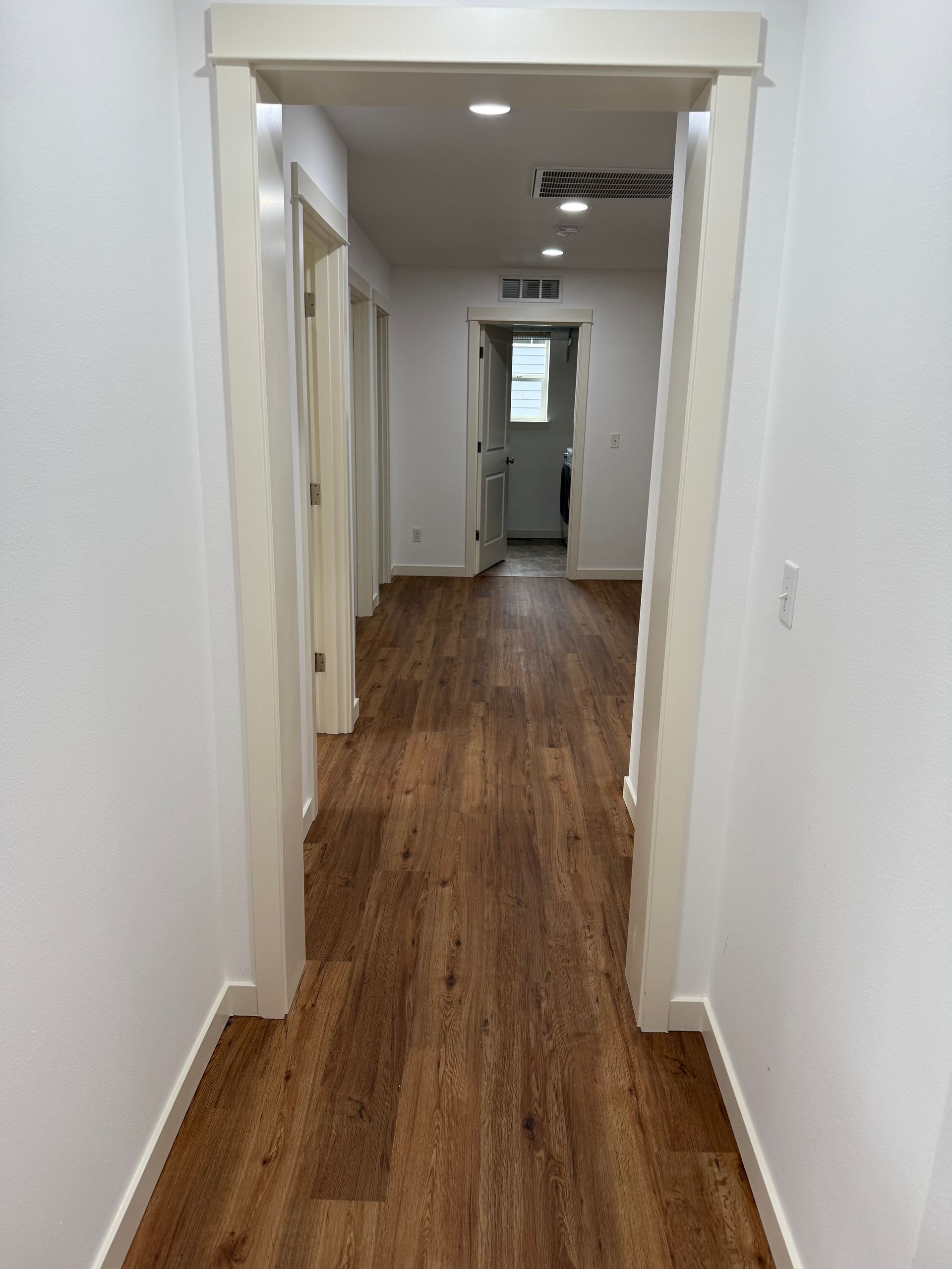 Hallway with wood floors, white walls, and doorways leading to rooms.