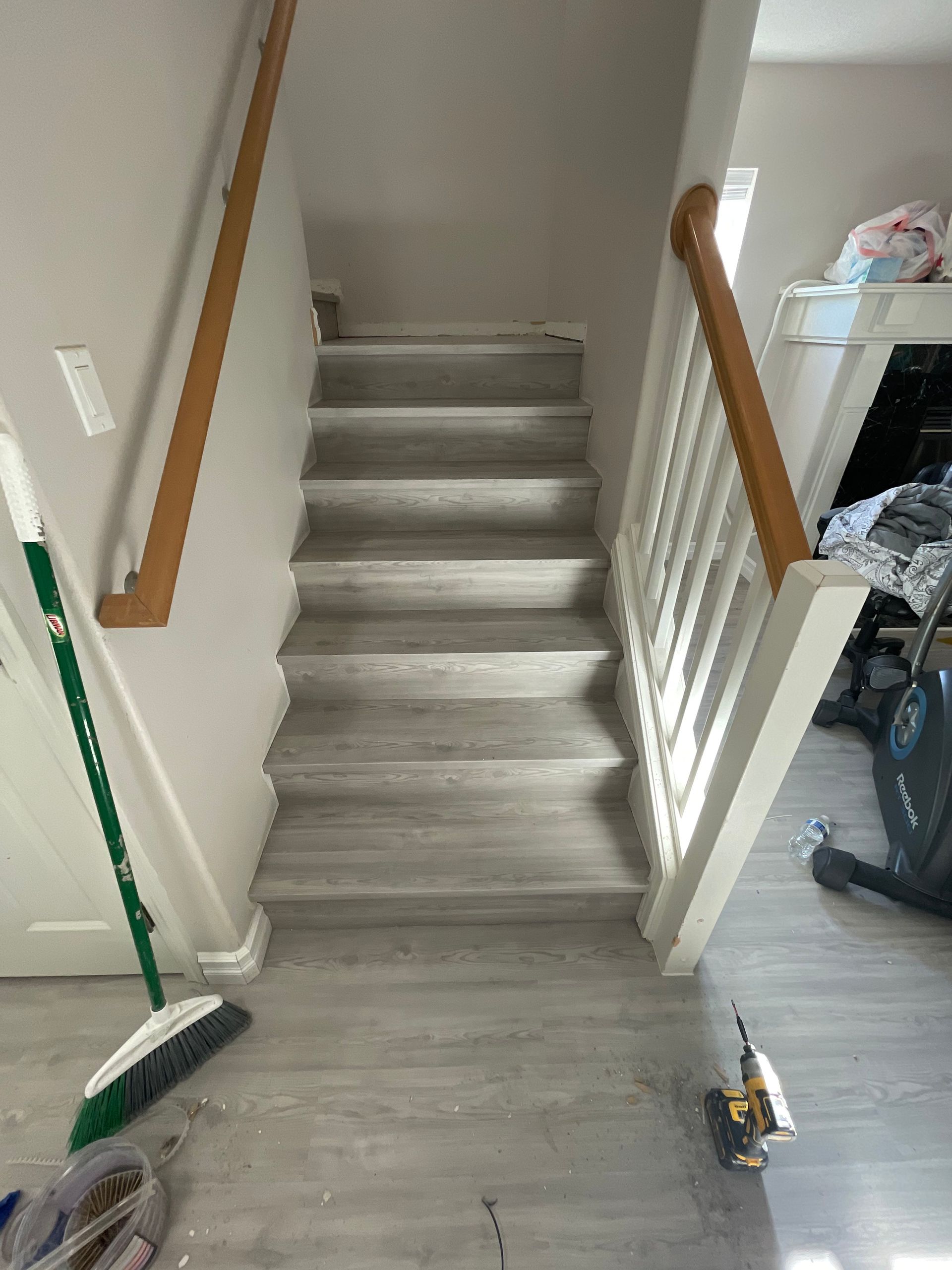 Staircase with gray flooring, wooden handrails, and white banisters. A broom and tools sit at the bottom.