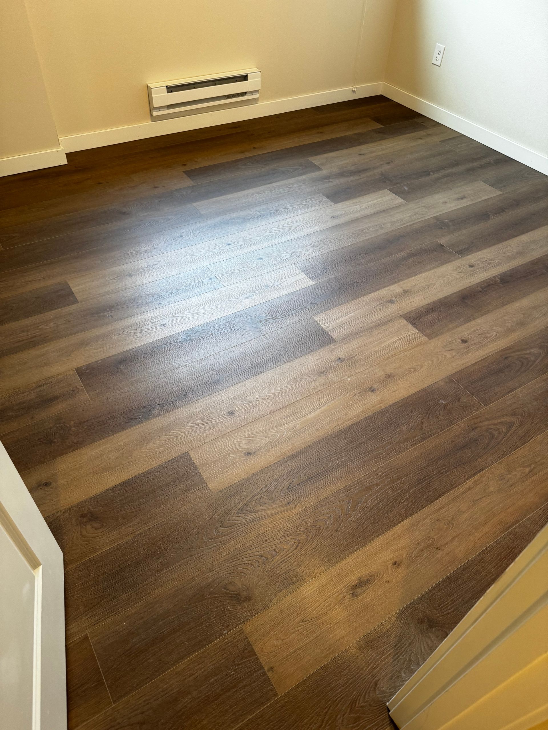 Room with brown wood-look flooring, white trim, and a wall vent.
