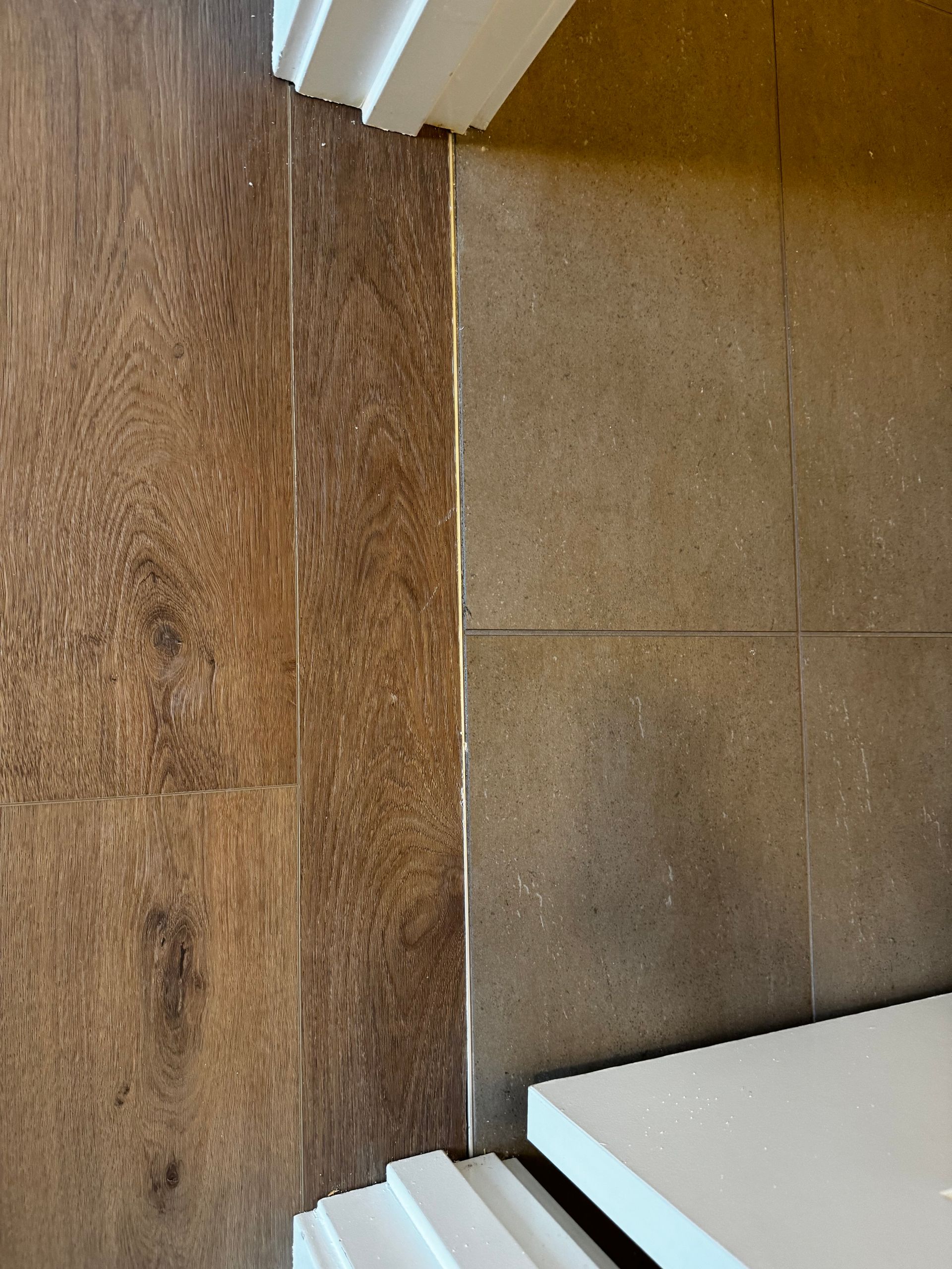 Wood floor meets tile floor, separated by a thin strip. White trim is visible.