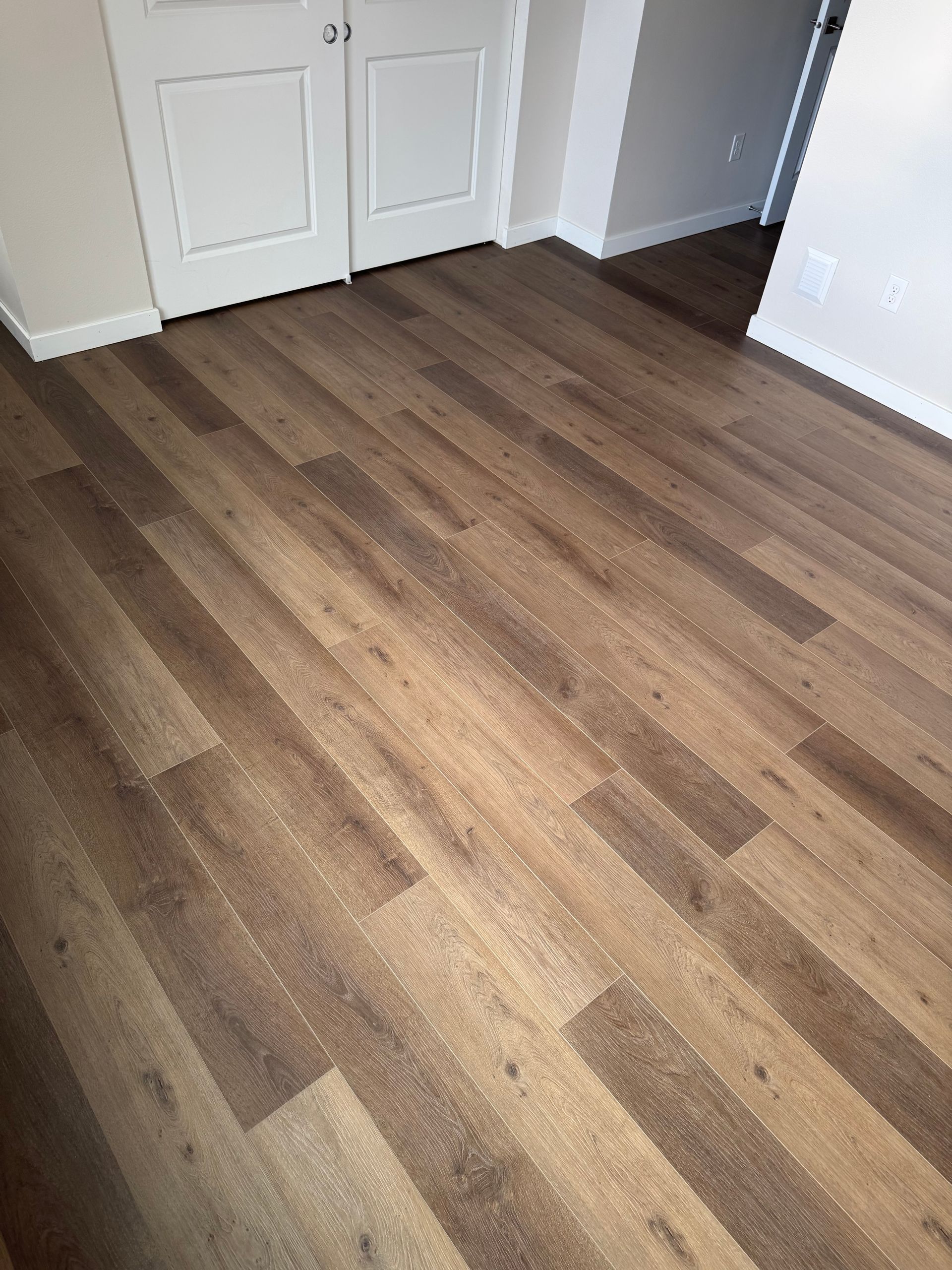 Brown wood-look flooring with white trim and doors in a room.