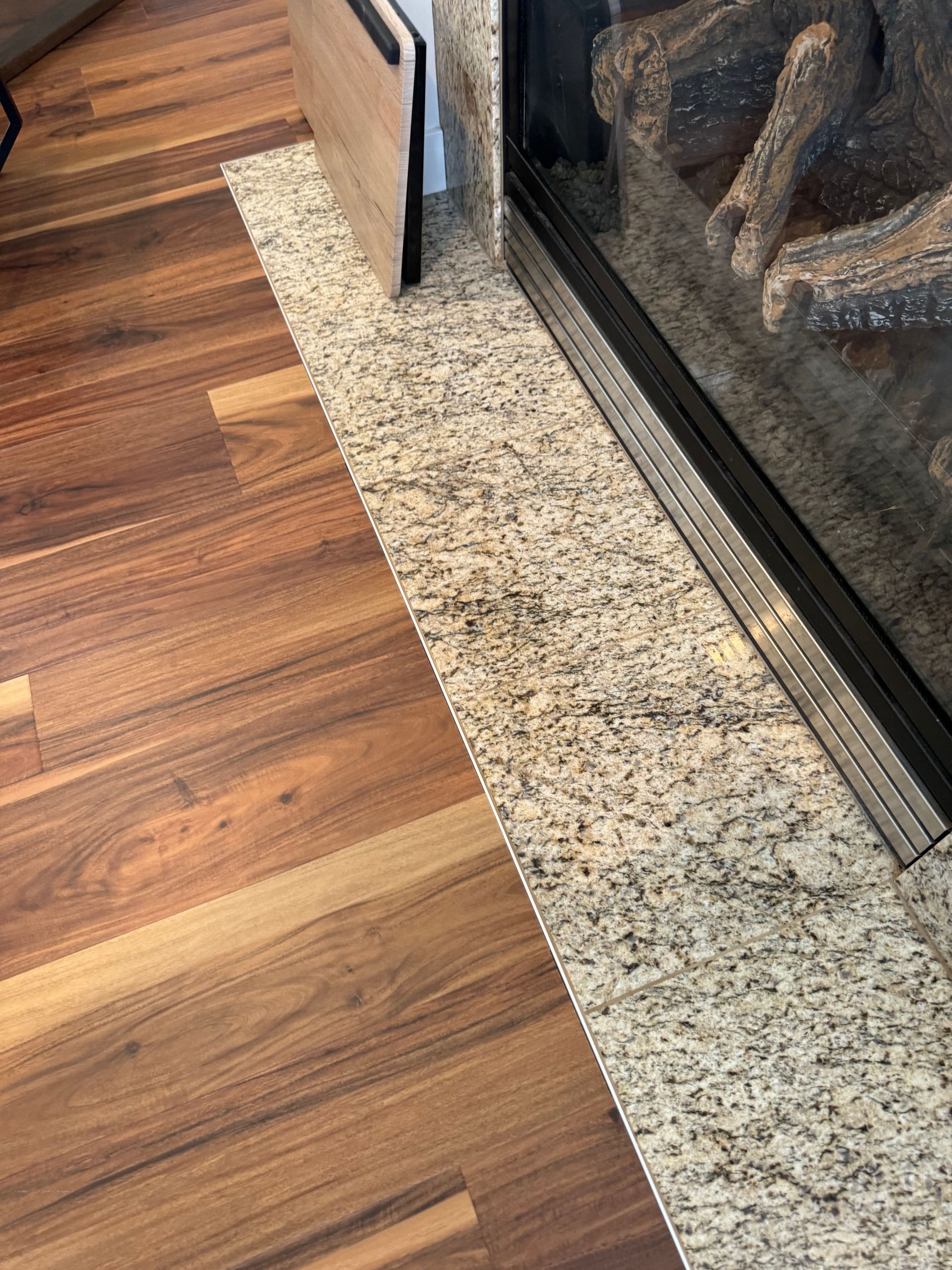 Brown wood floor meets granite hearth next to a fireplace.