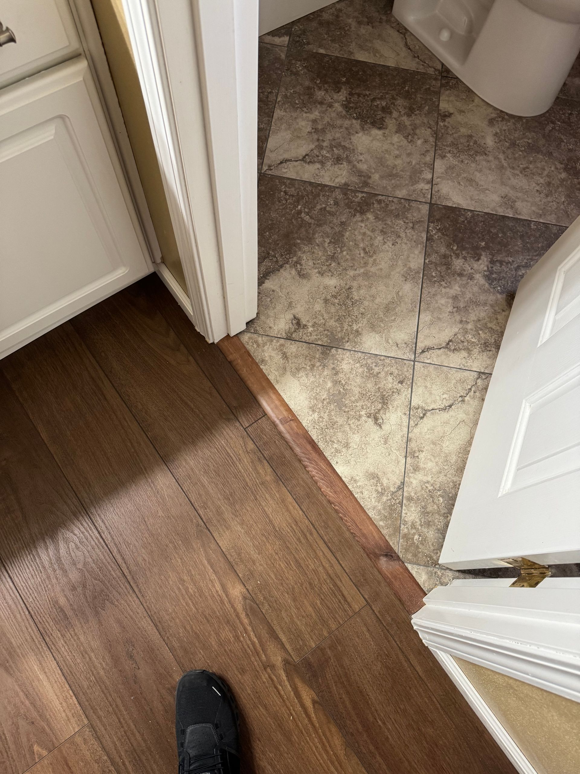Bathroom floor with two types of flooring: dark wood and patterned beige.
