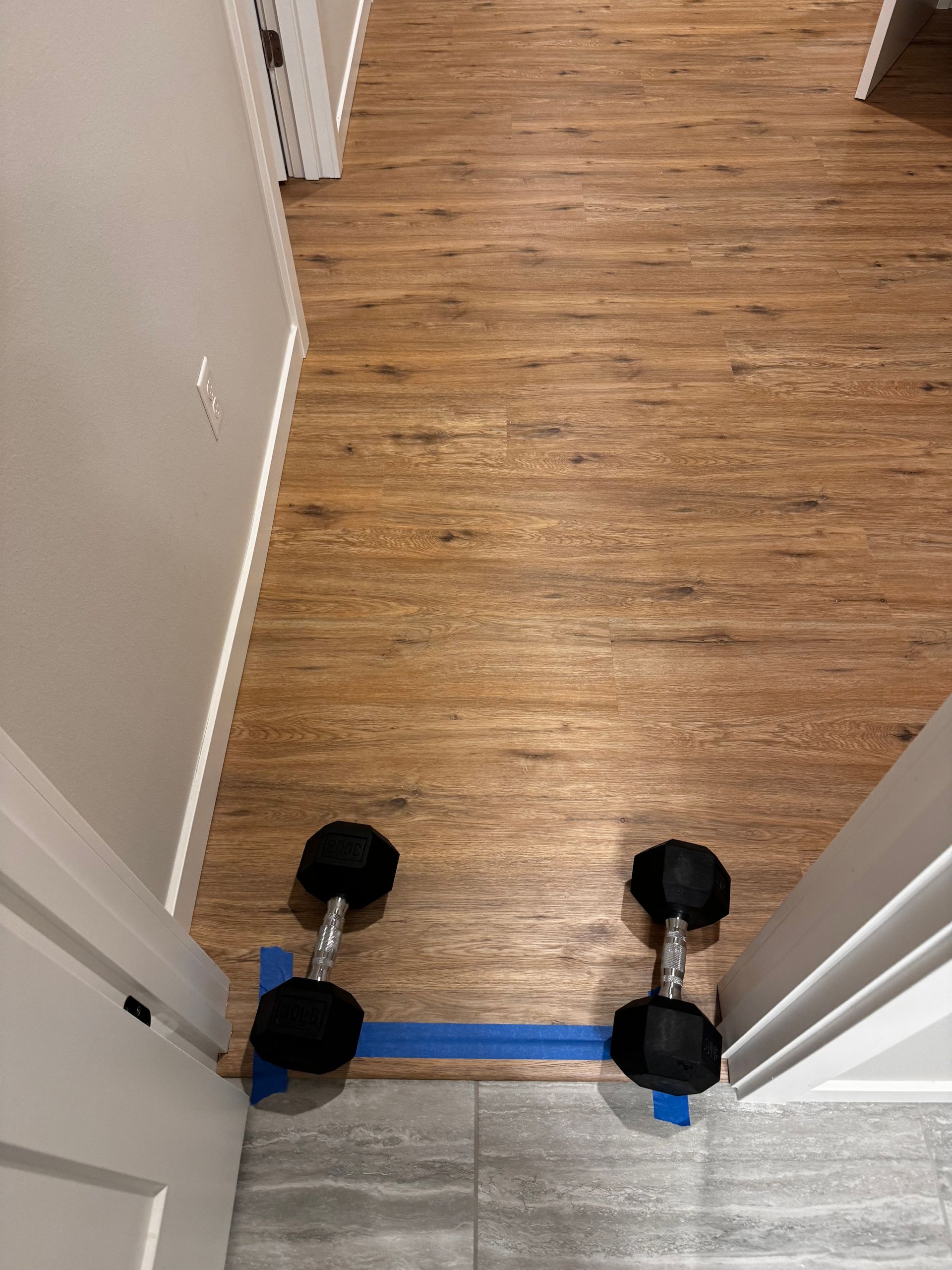 Two dumbbells are taped together in a doorway to block access, on a wood floor and tiled entryway.