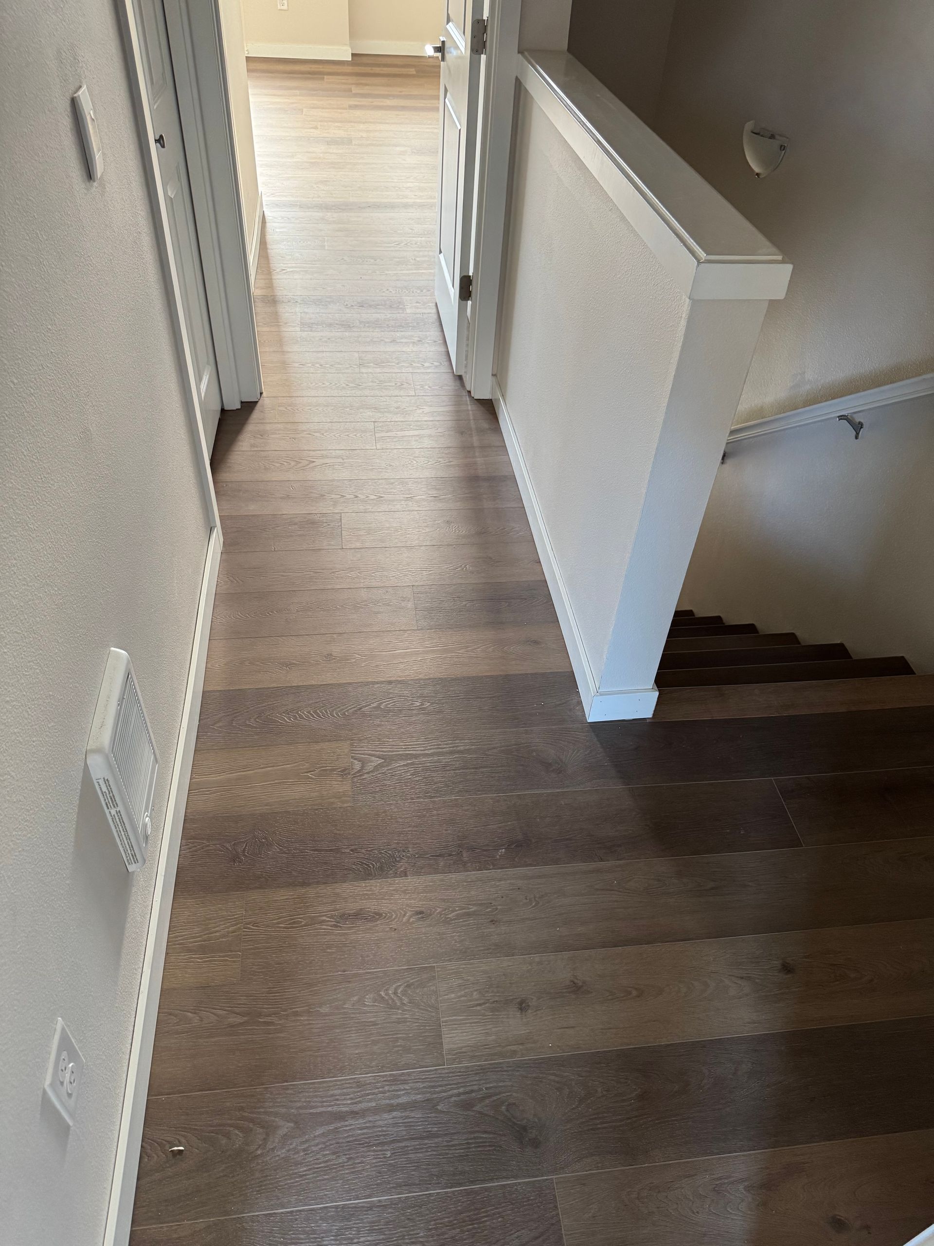 Hallway with wood-look flooring, stairs to the right, white walls, and a closed door at the end.