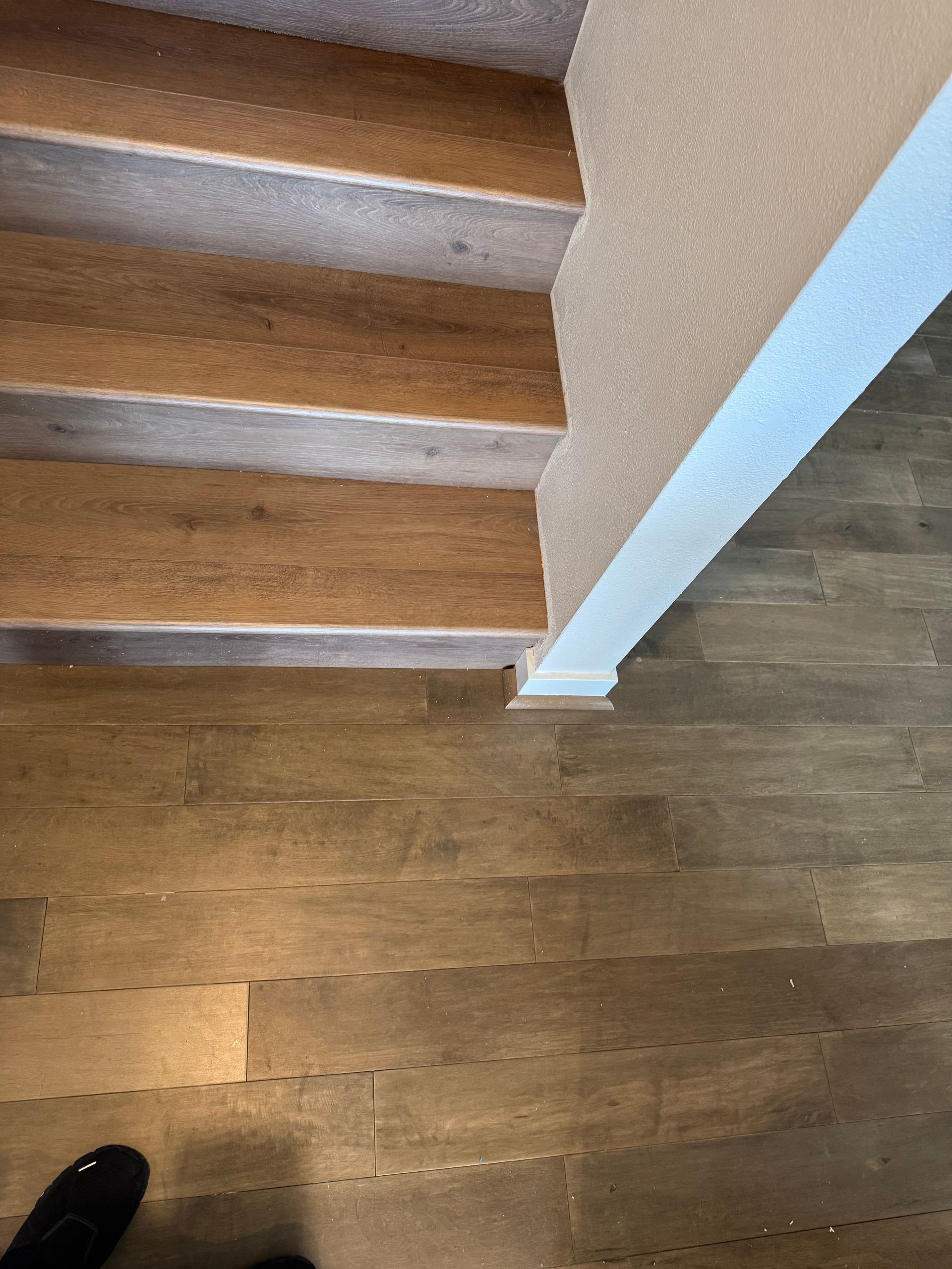 Wooden stairs leading up from a darker-toned wooden floor, with a white wall on the right.