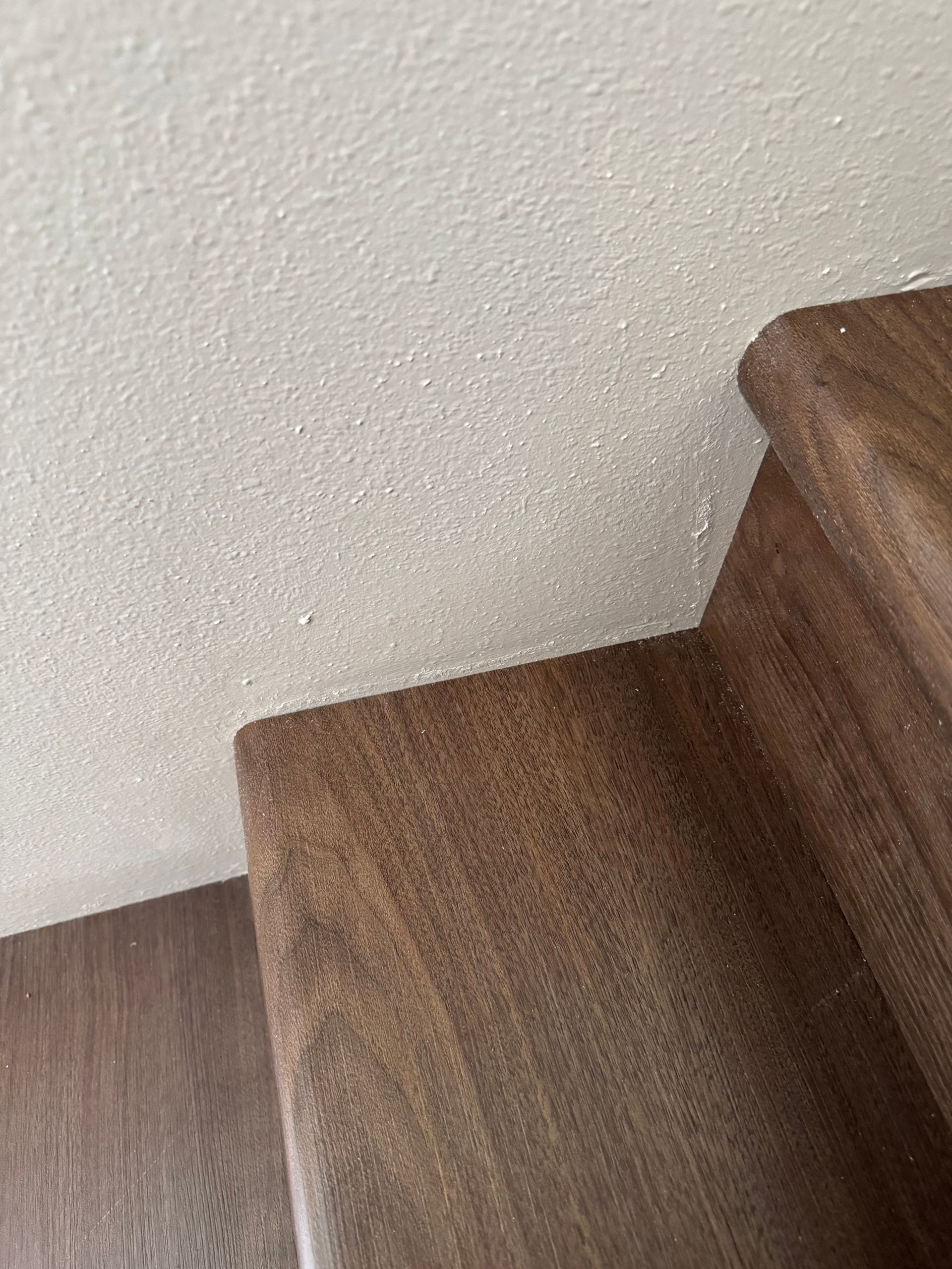 Wooden staircase with brown treads and white textured wall.