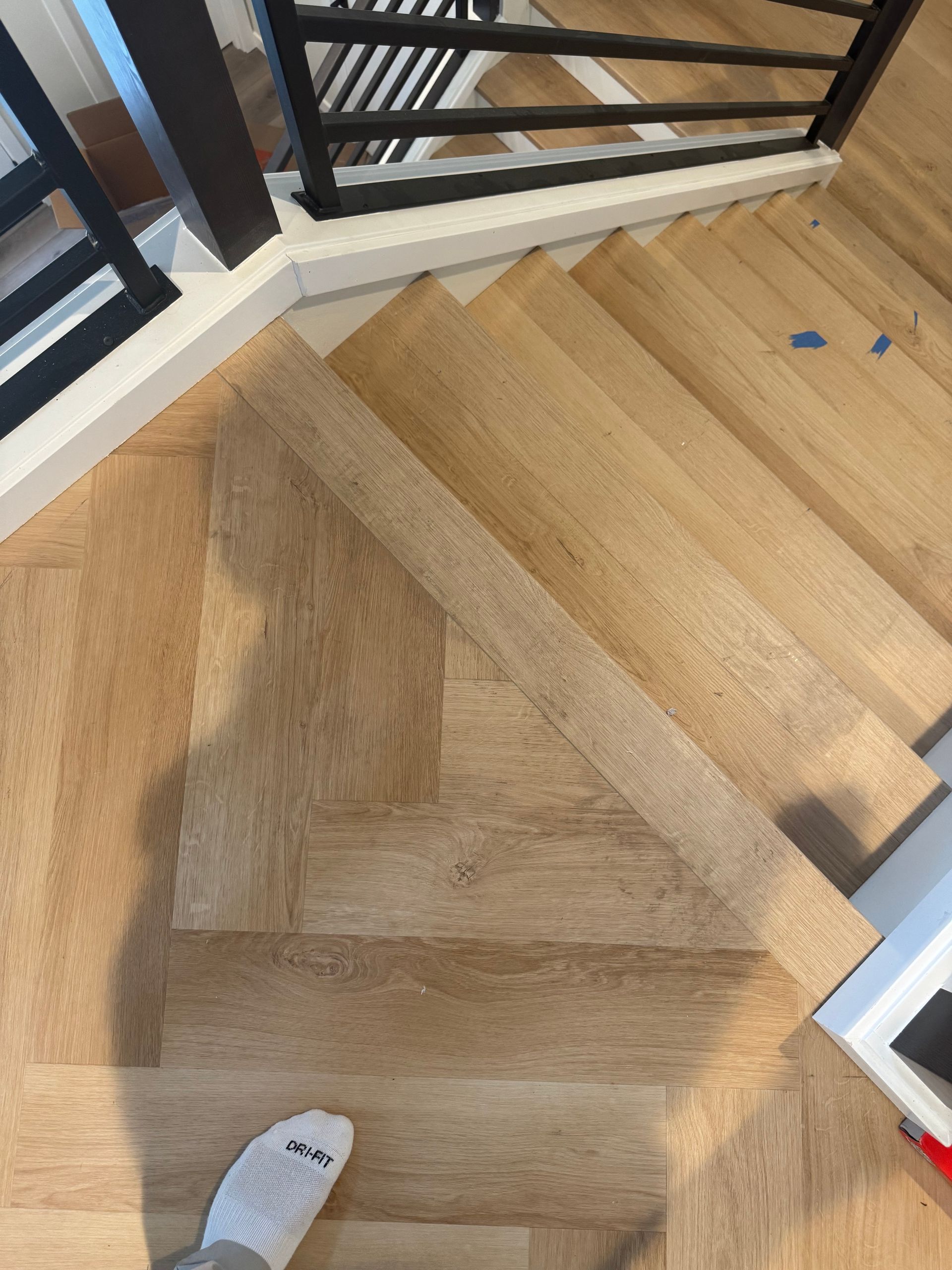 Wooden staircase with herringbone pattern flooring. A foot in a sock is visible.
