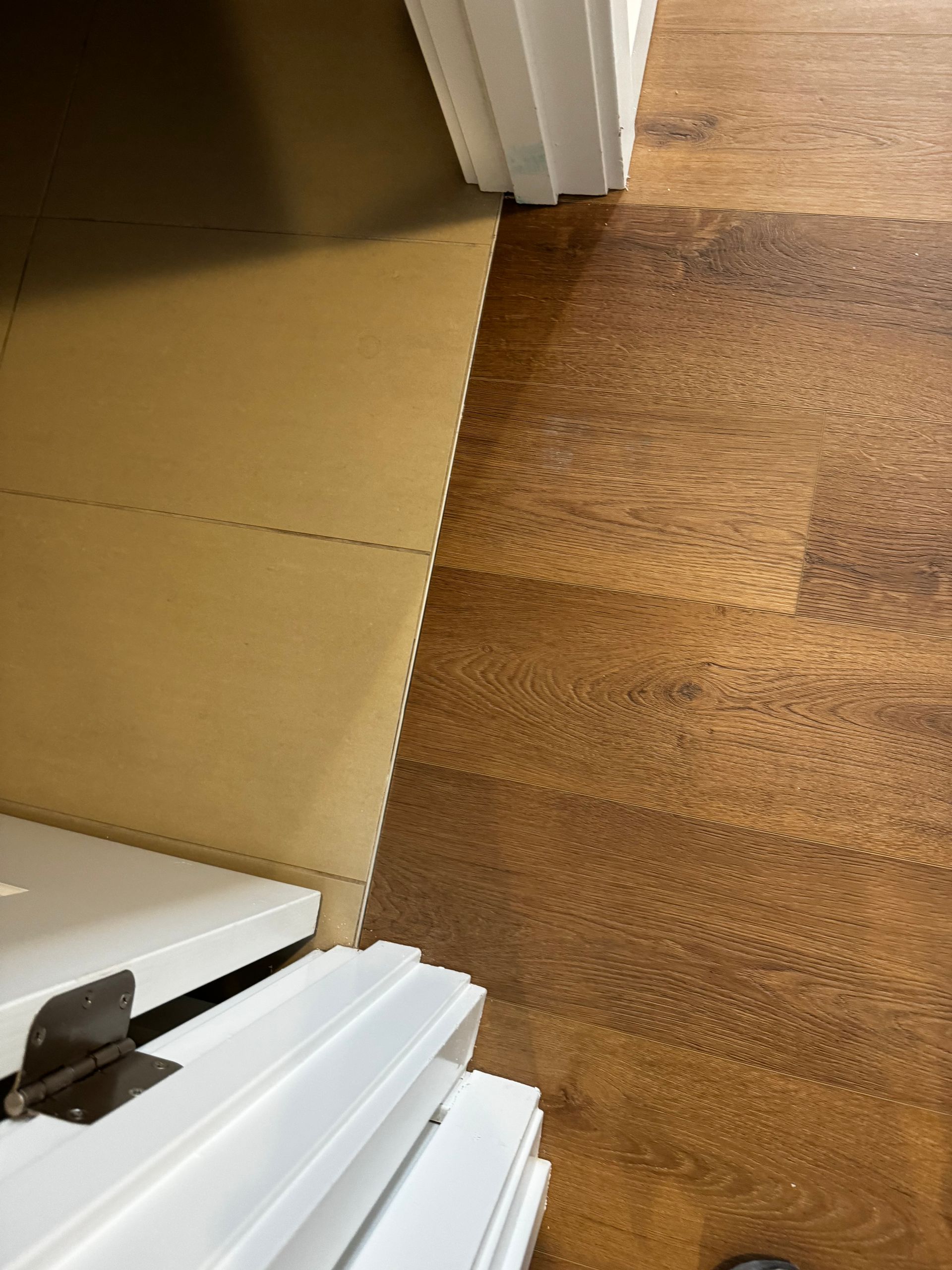 Floor transition: light tan foam tiles next to dark wood-look flooring, with white door frame at top and bottom.