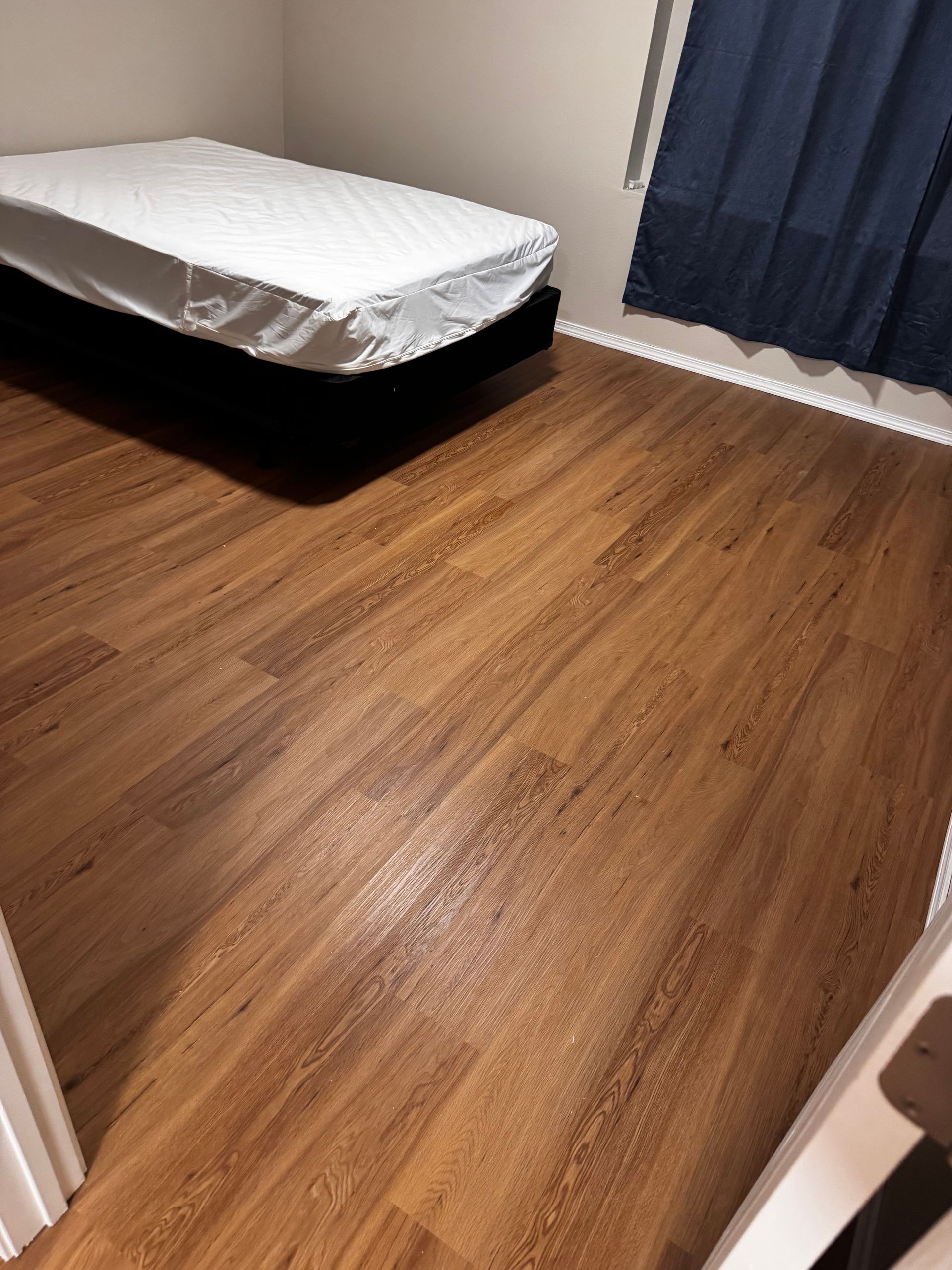 Bedroom with a bed, wood-look flooring, and a blue curtain.