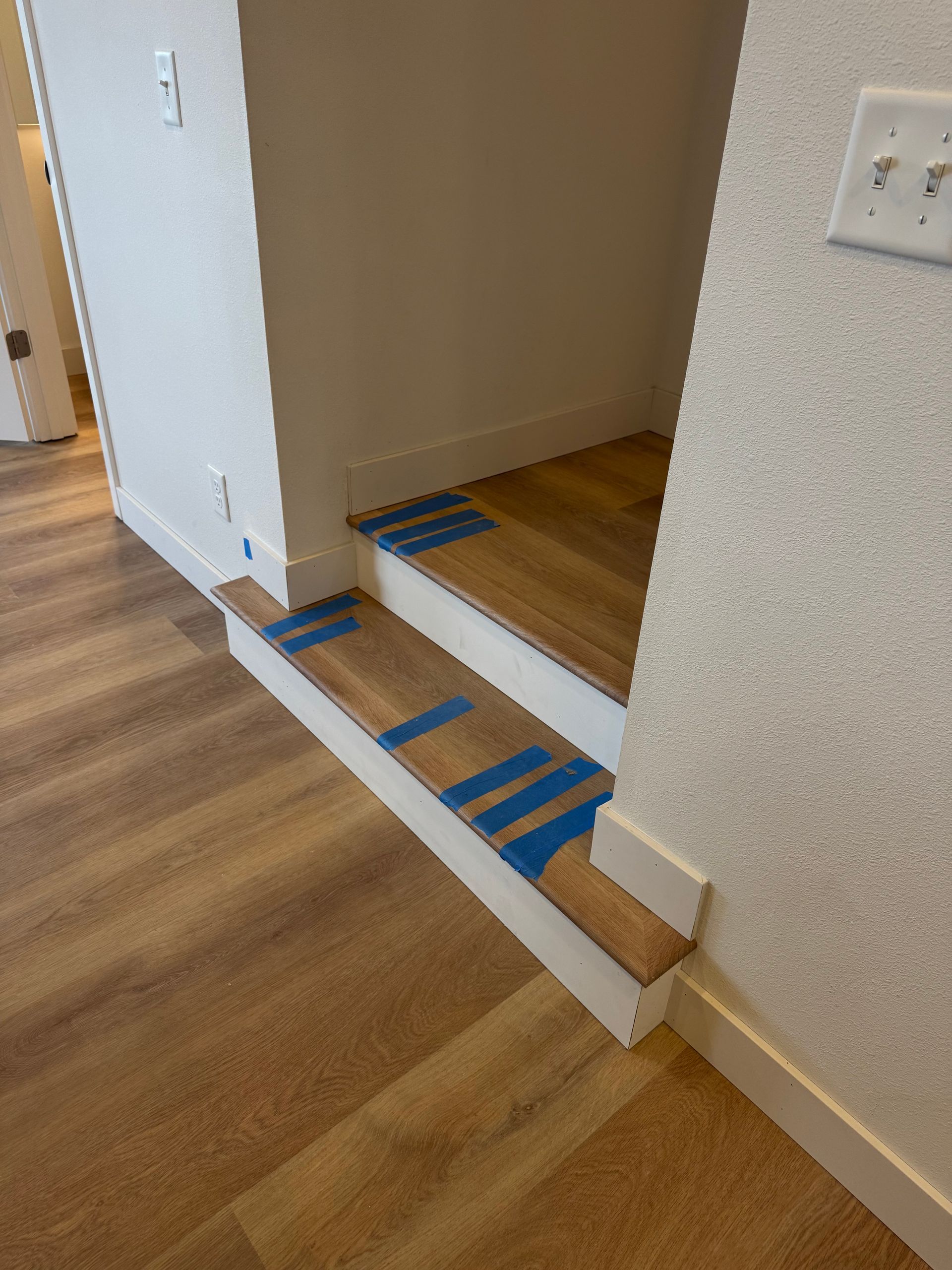 Staircase with wood steps and white risers; blue tape is on the steps.