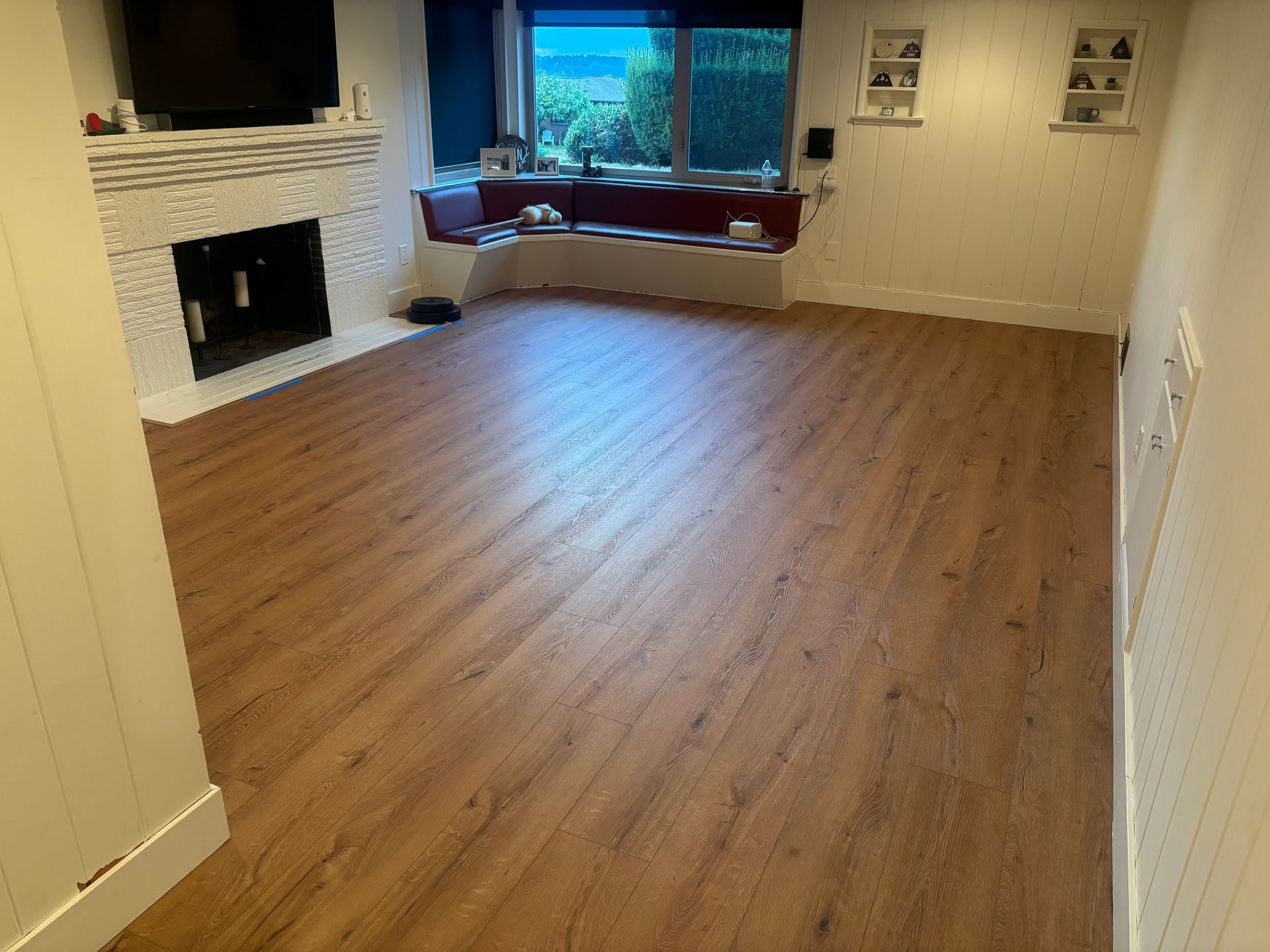 Empty living room with brown wood-look flooring, white fireplace, and window seat with a view.
