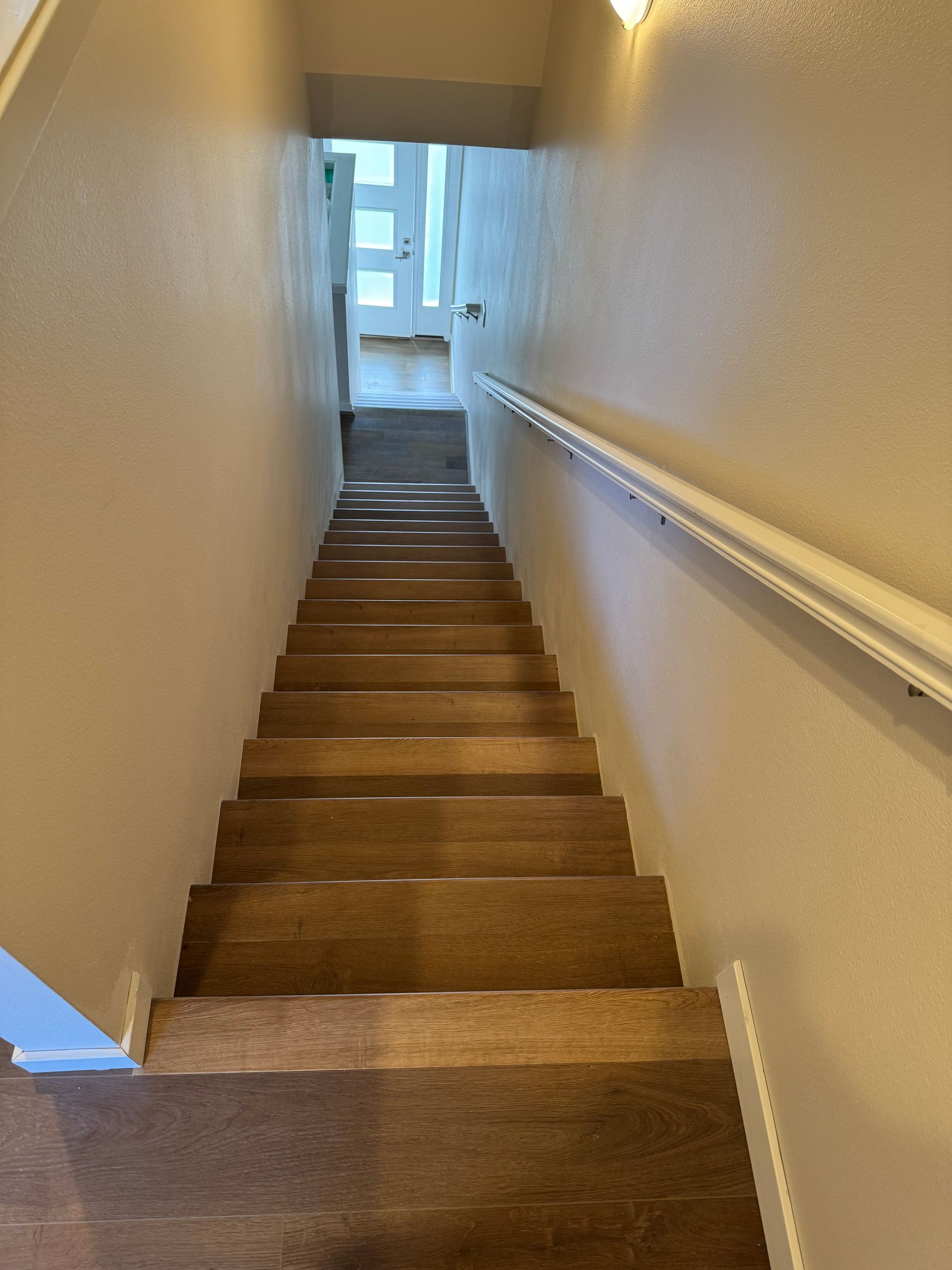 Staircase leading downwards. Wooden steps, white handrail on right, white walls.