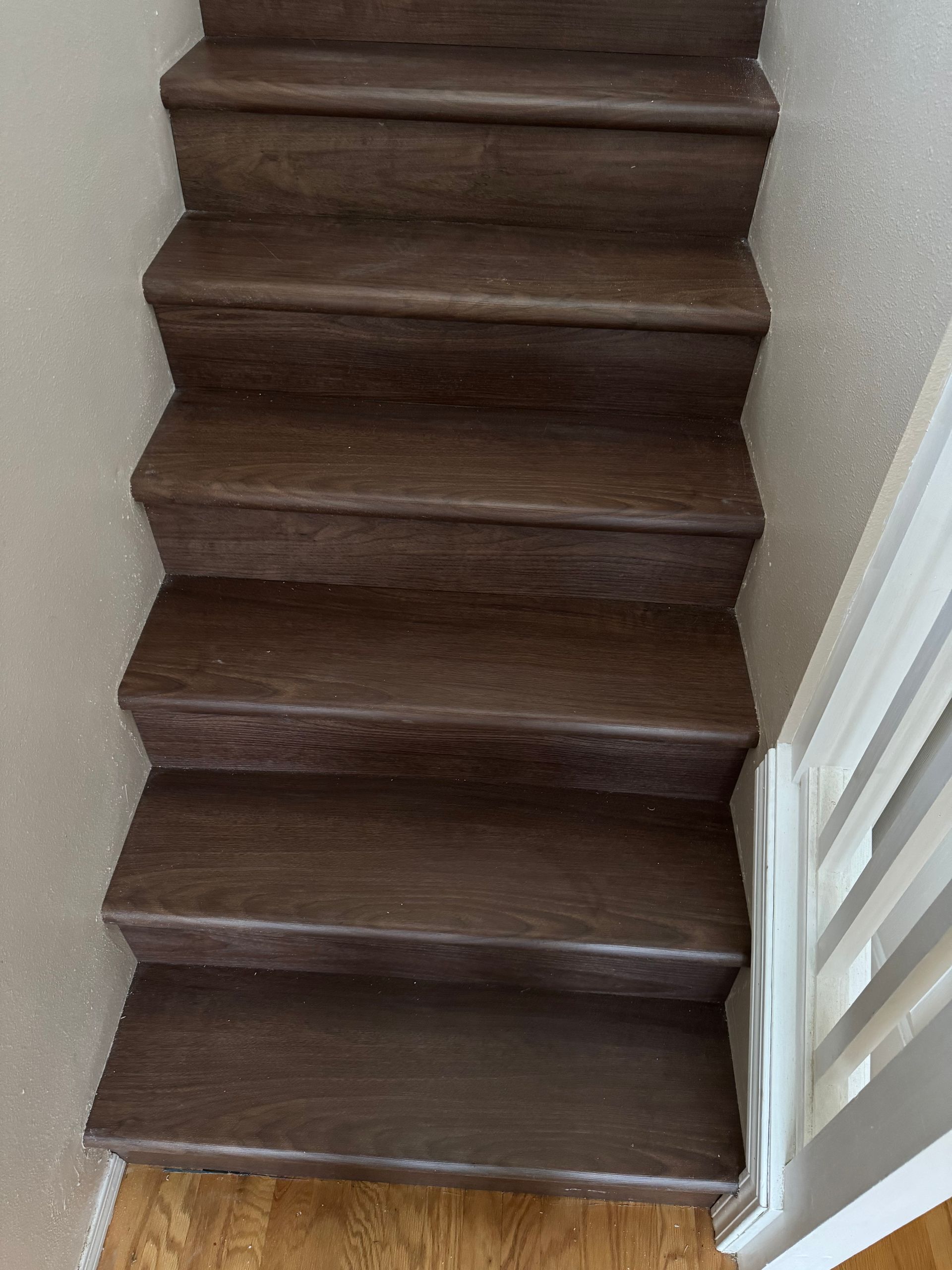 Wooden stairs with dark brown treads and beige carpet sides, leading upwards with a white banister on the right.