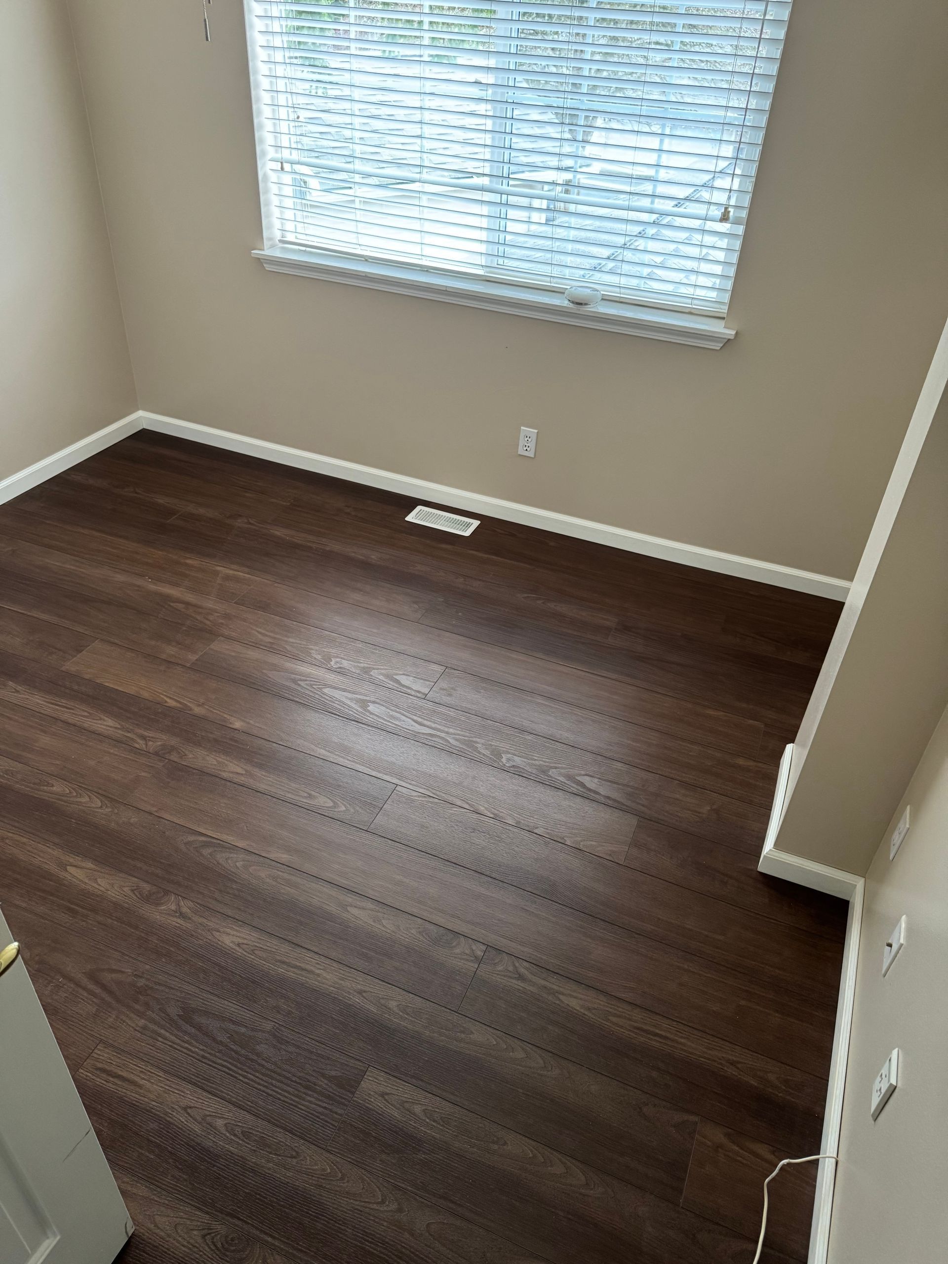 Empty room with dark wood floor, tan walls, and a window with blinds.