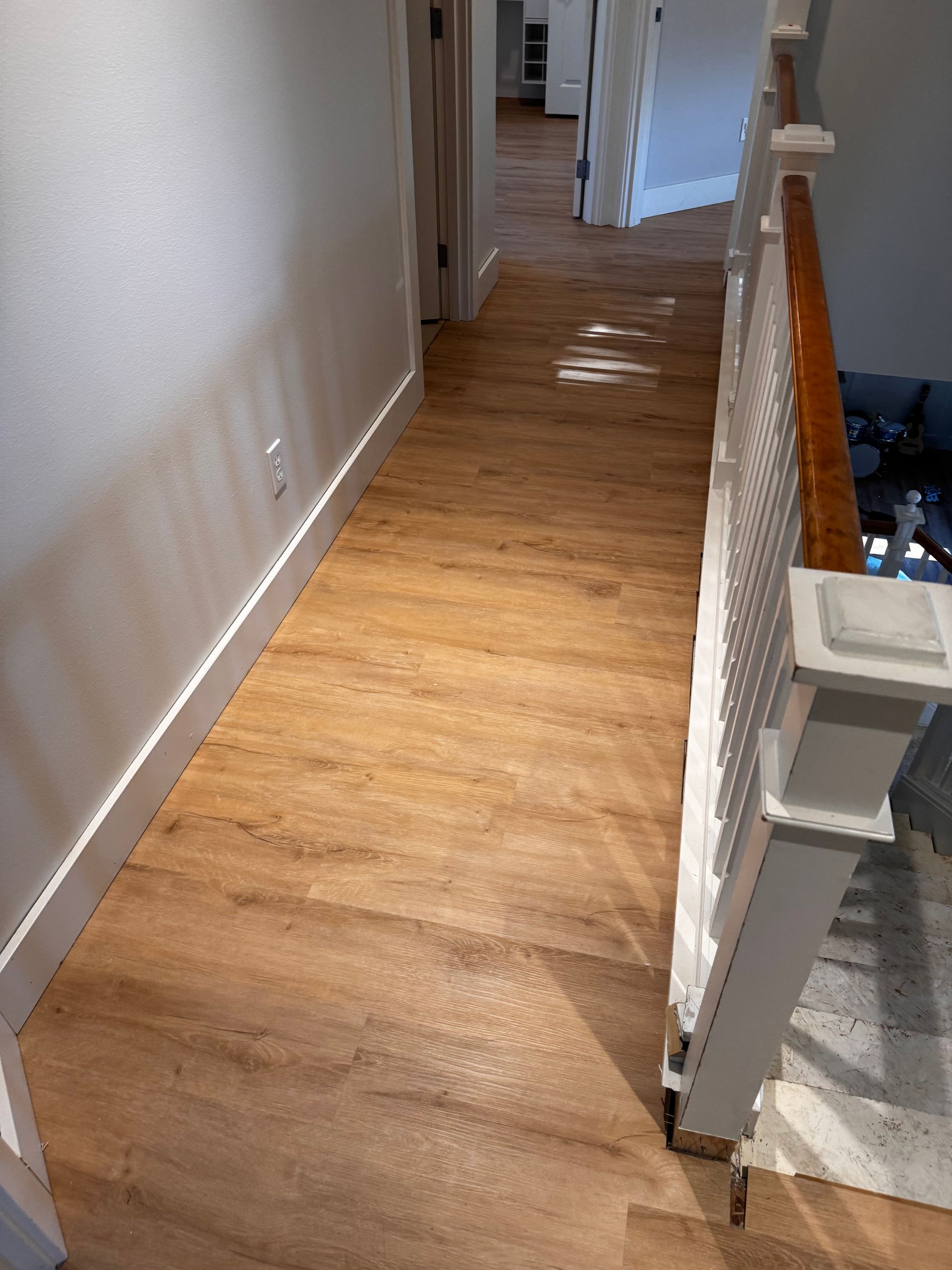 Hallway with wood-look flooring, white walls, and a staircase with a white railing and brown handrail.
