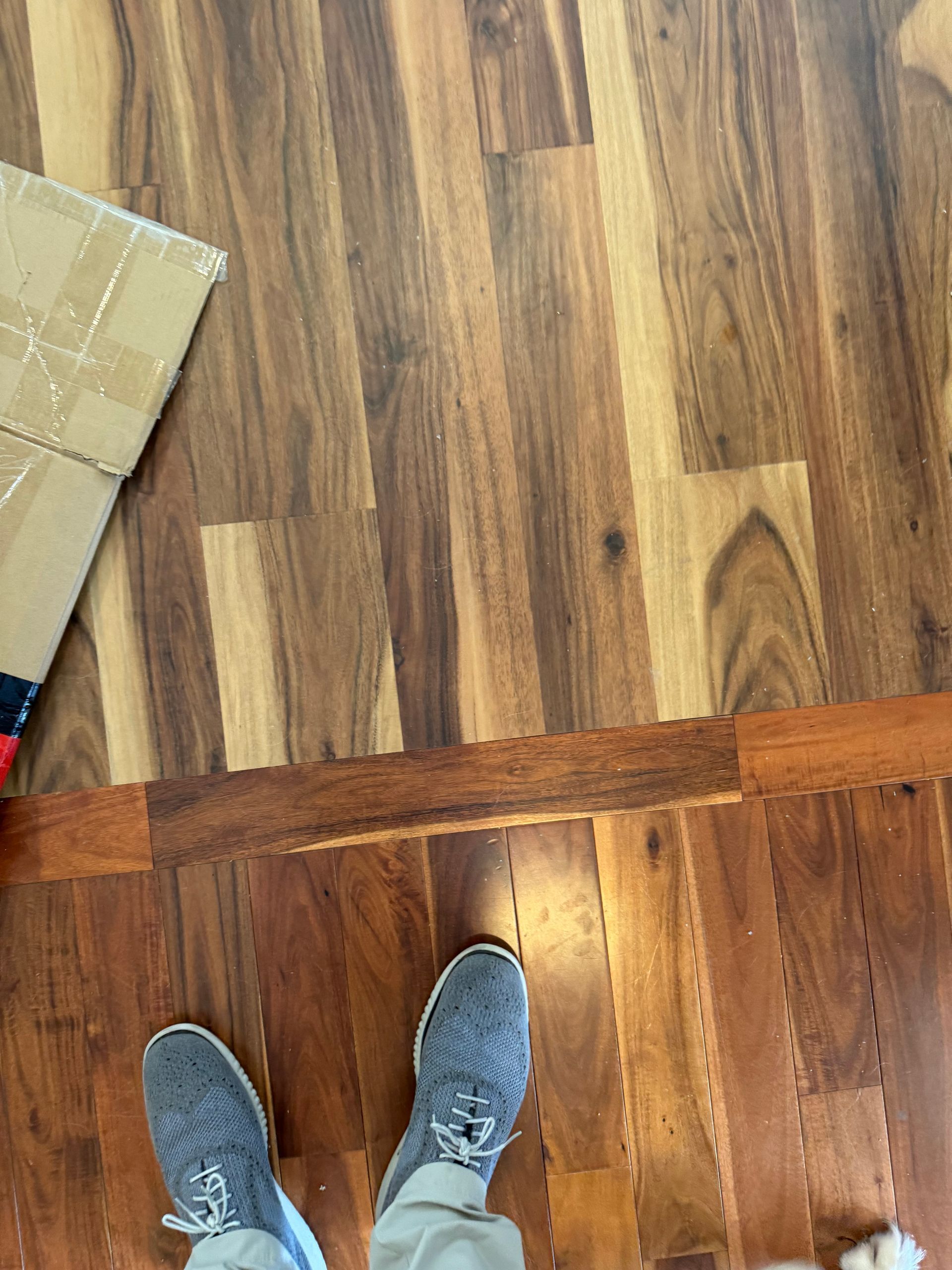 Person standing on wood flooring, wearing gray sneakers, next to a cardboard box.
