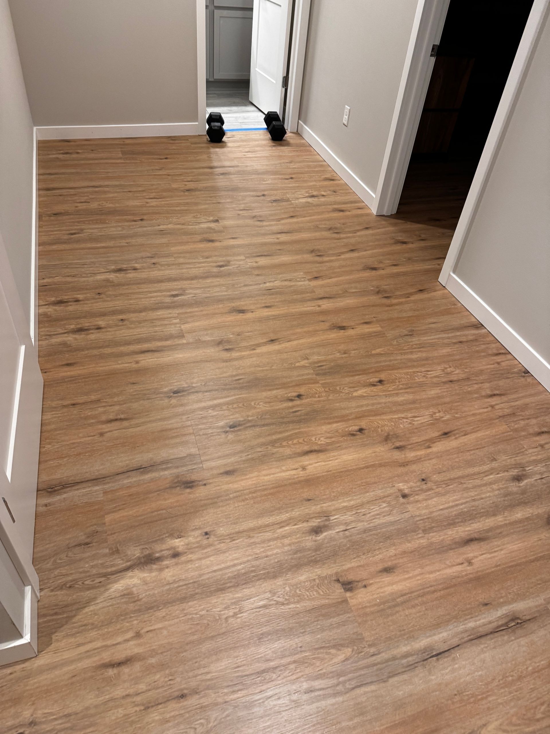 Hallway with wood-look flooring and white trim. Doors are visible at the end of the hall.