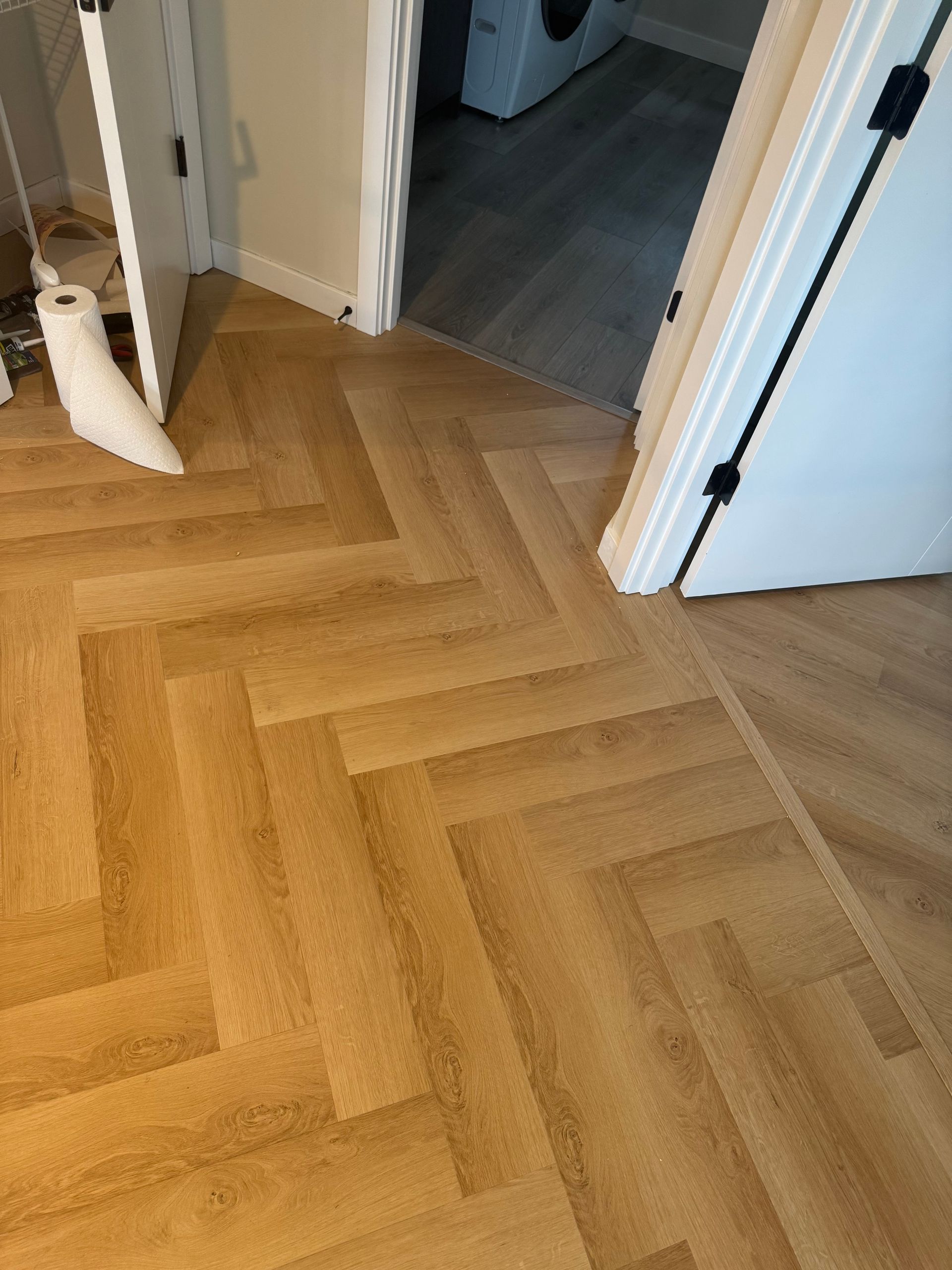 Herringbone pattern wood-look flooring. Light brown planks are in a zig-zag design. Doorways in view.