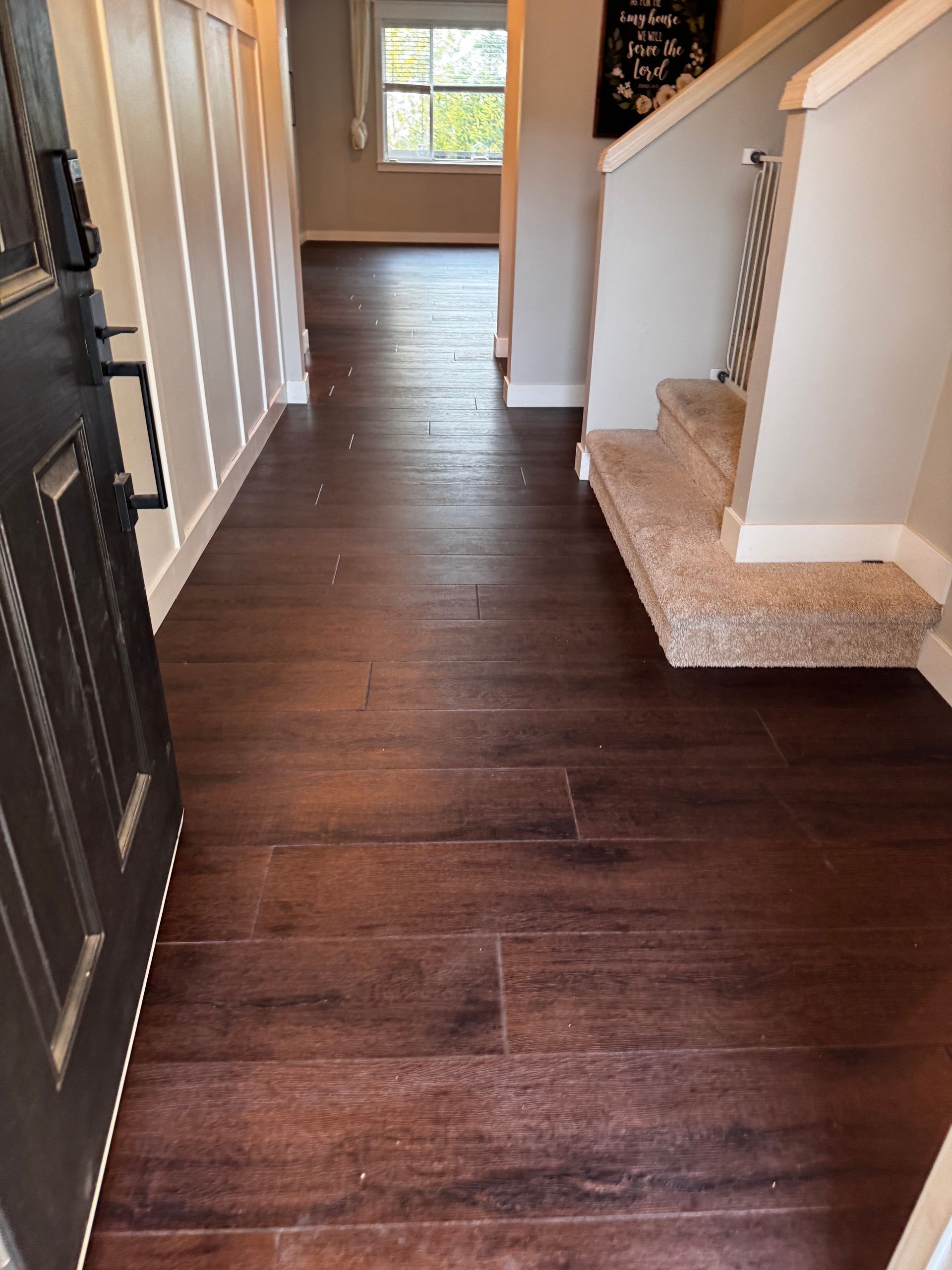 Dark wood-look flooring in a home entry. The front door is on the left, stairs on the right.