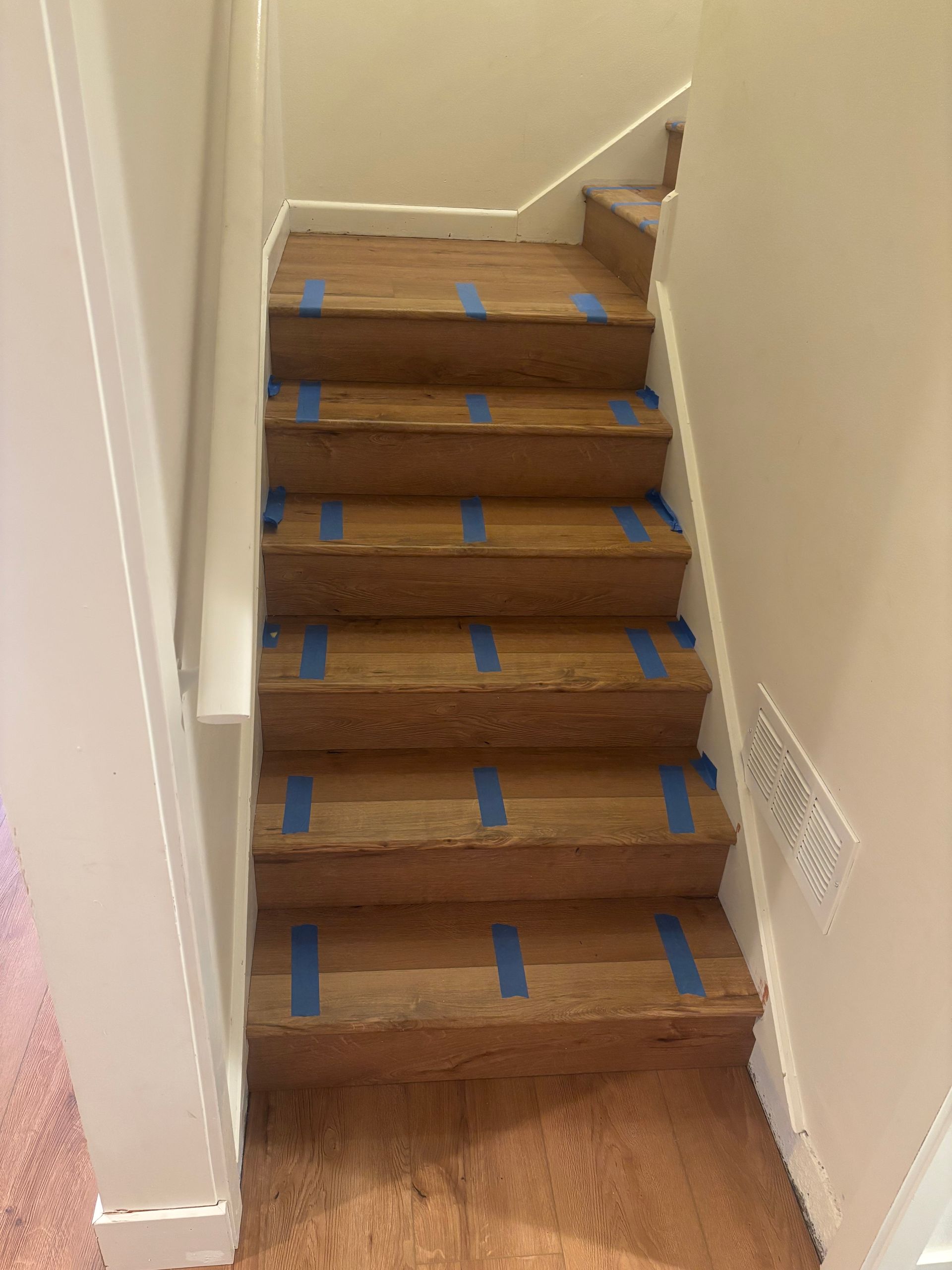 Wooden staircase with blue tape on treads.  White trim and walls.