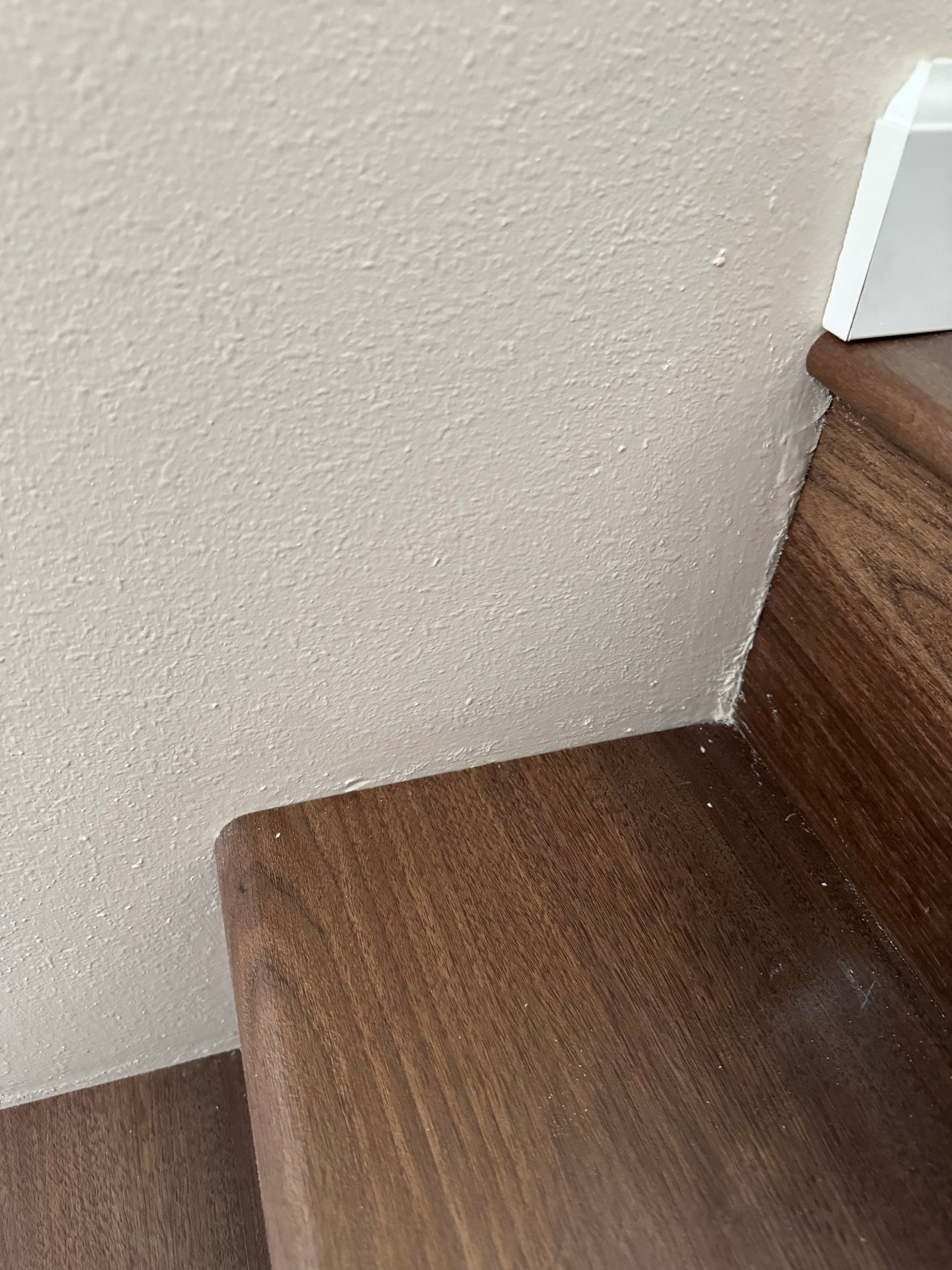 Wooden stair treads and wall with textured finish, near white trim.