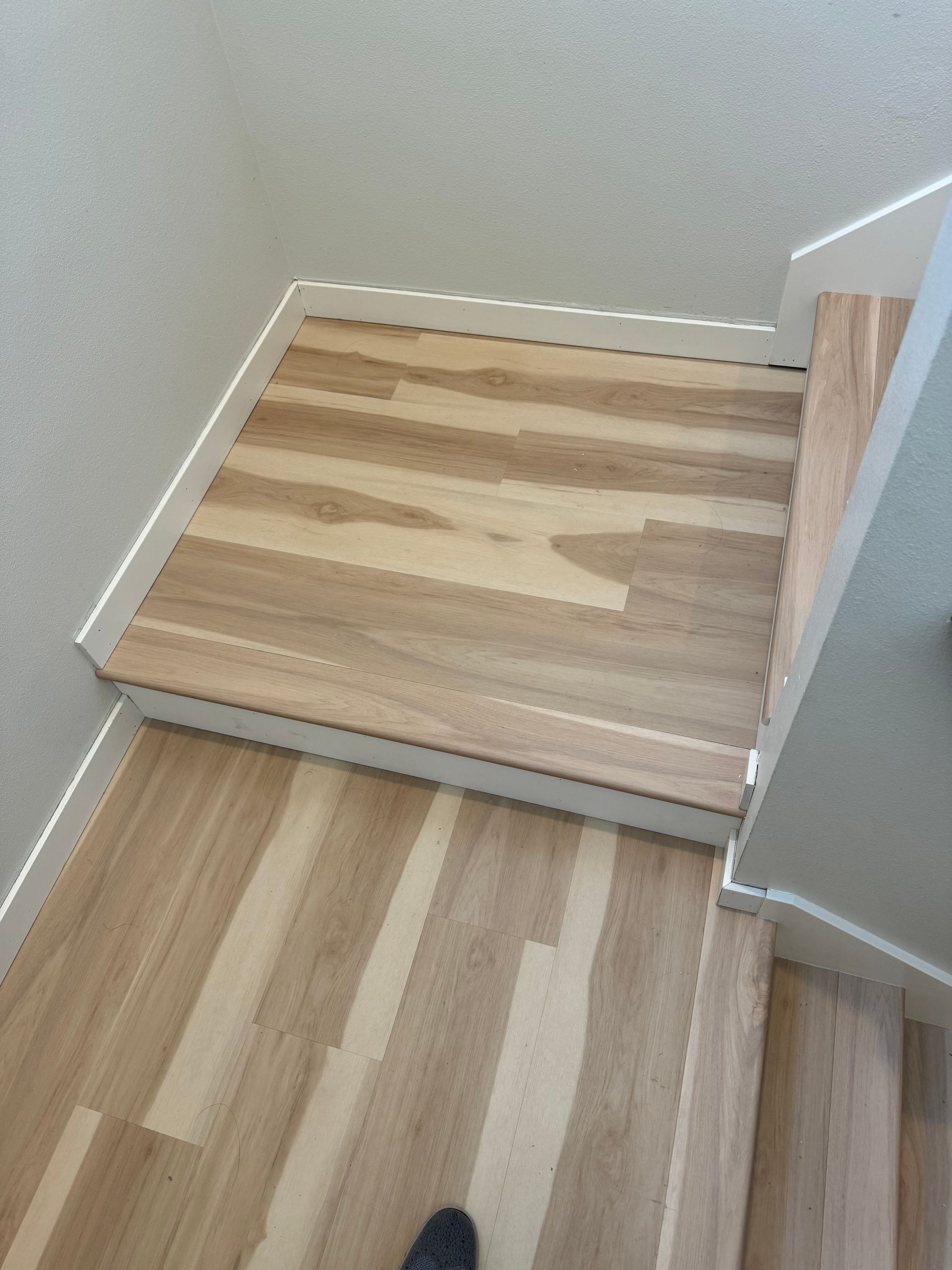 Wooden stairs and landing with white trim, viewed from above.