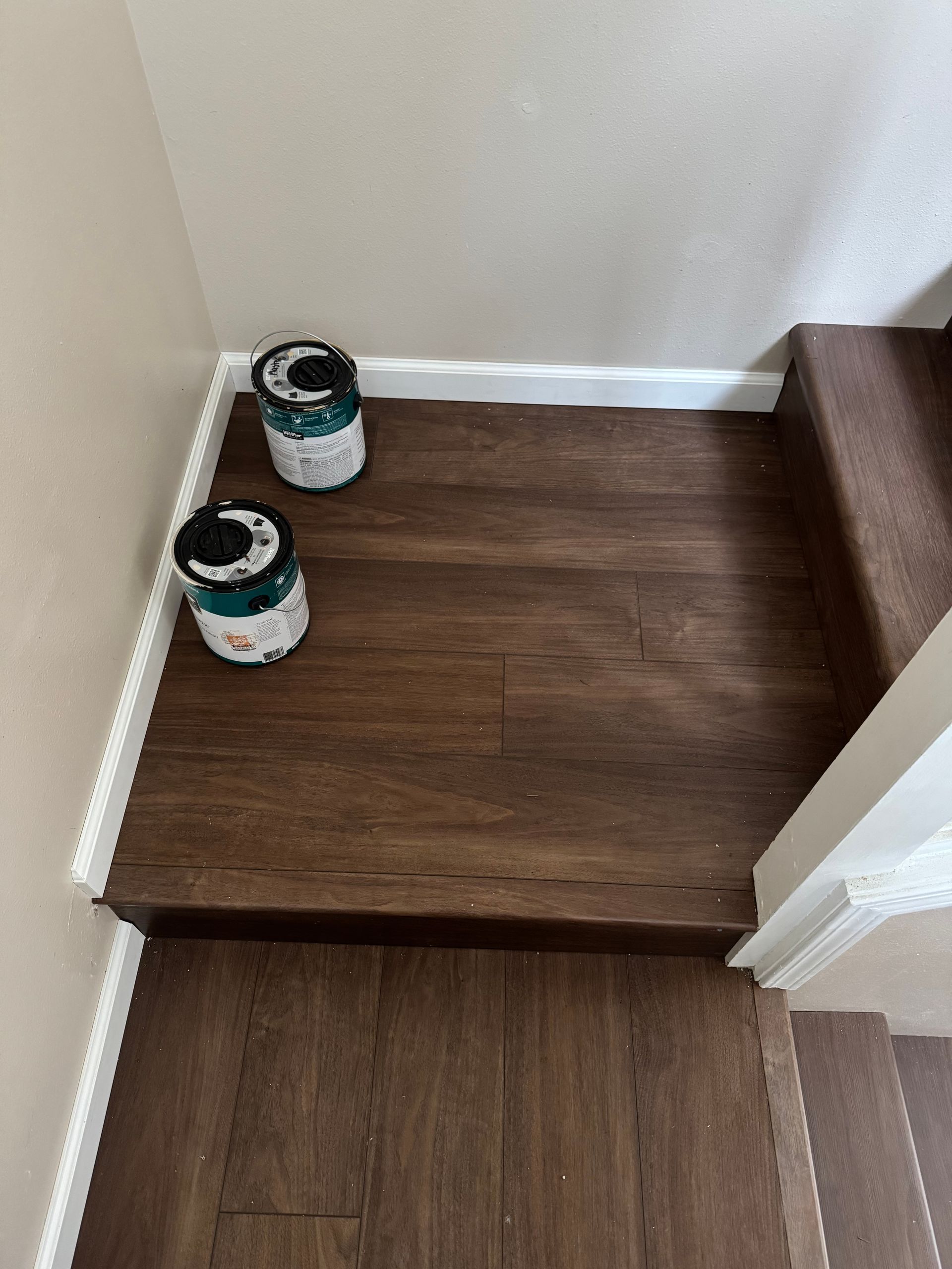 Stairwell with dark brown flooring. Two paint cans sit on the landing, next to white trim.