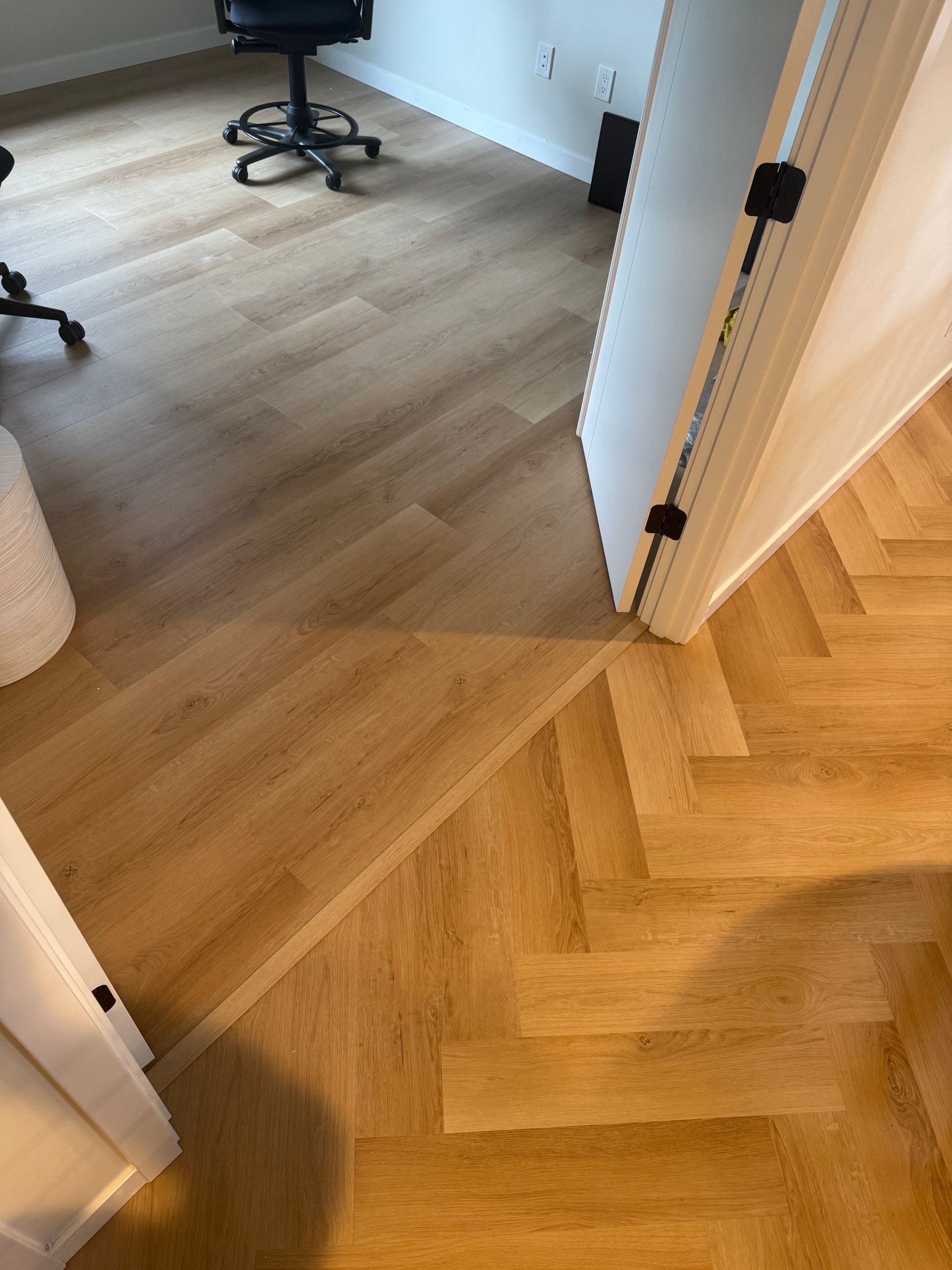 Hardwood floors: a straight plank design transitions to a herringbone pattern. A doorway is in the frame.