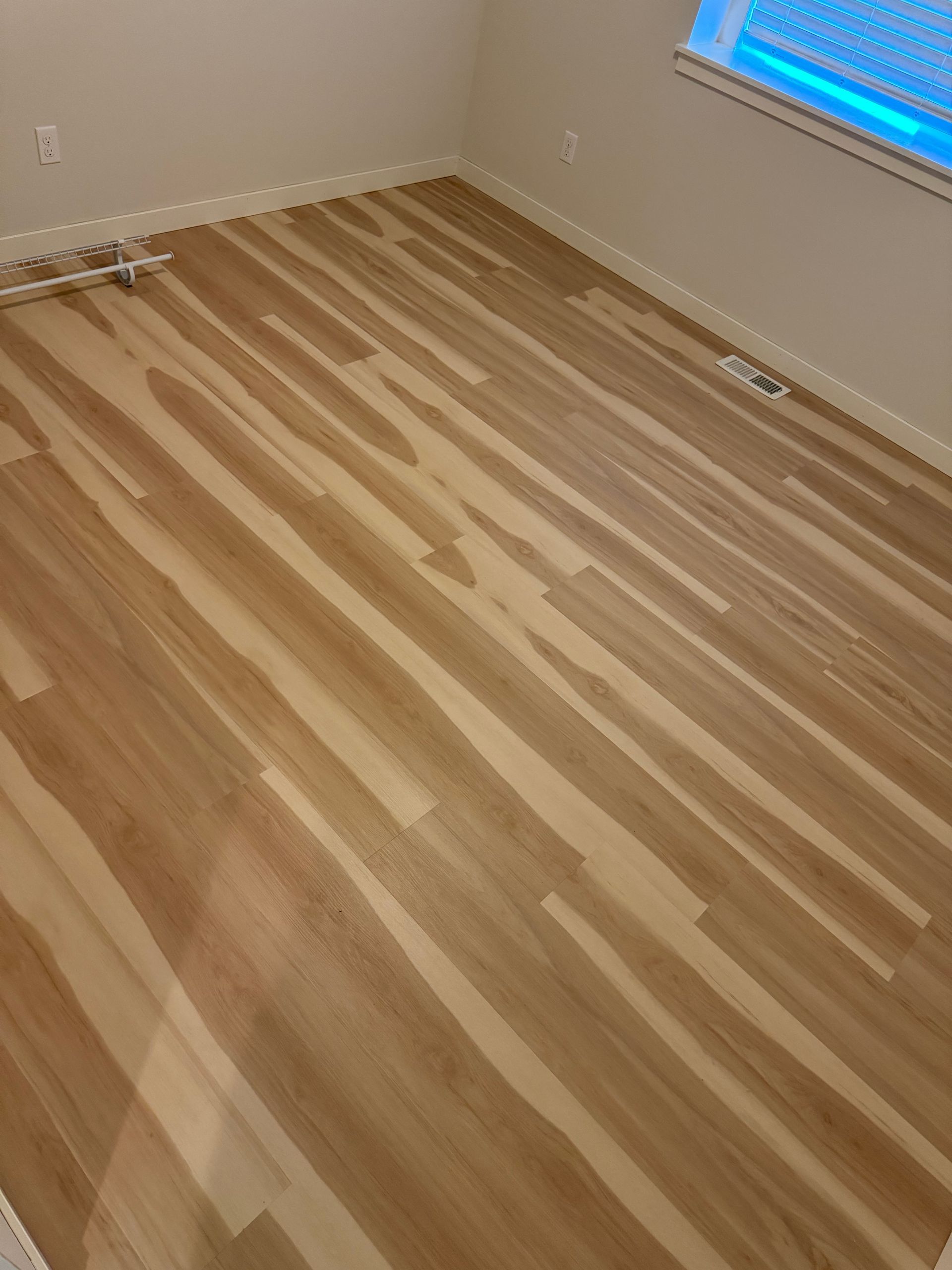 Wooden plank flooring in a room with a window, white walls, and baseboards.