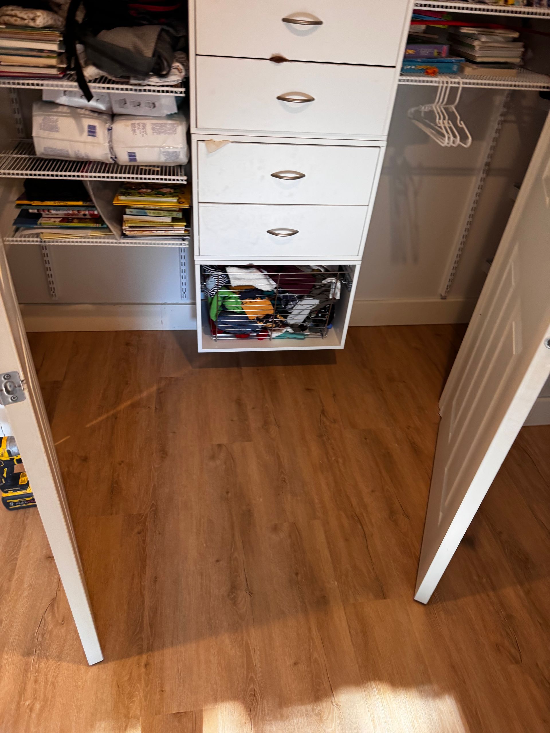 A closet with a white dresser, shelves, and wood-look flooring. Two doors are open on either side.