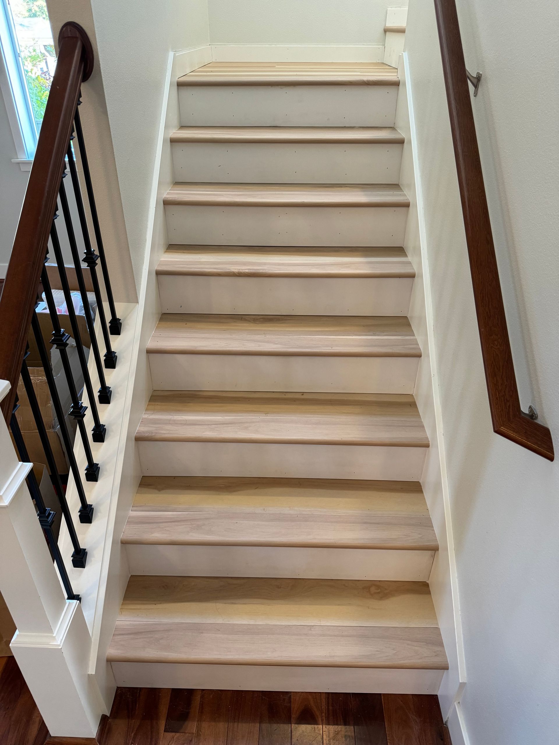Staircase with light-colored steps and white risers, wooden handrails on either side, and black iron balusters.