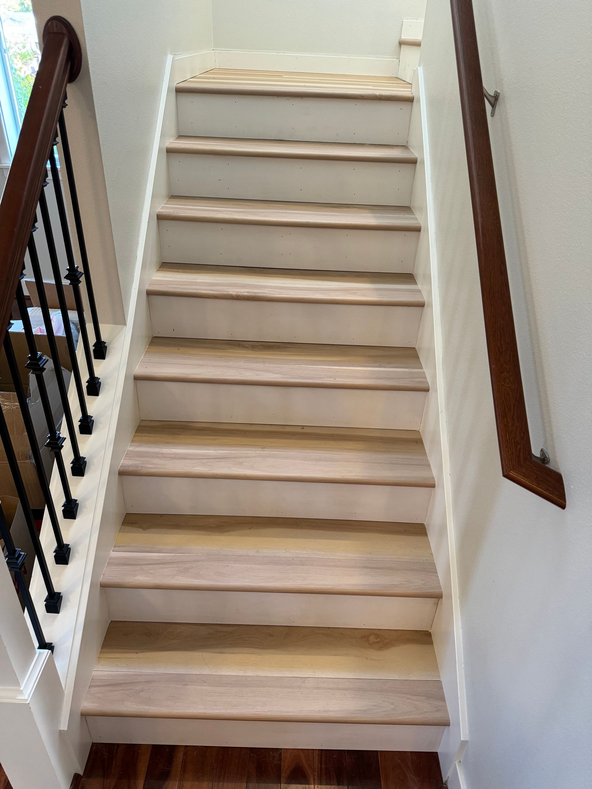 Staircase with wooden steps and white risers, black wrought iron railing on one side and a wooden handrail on the other.