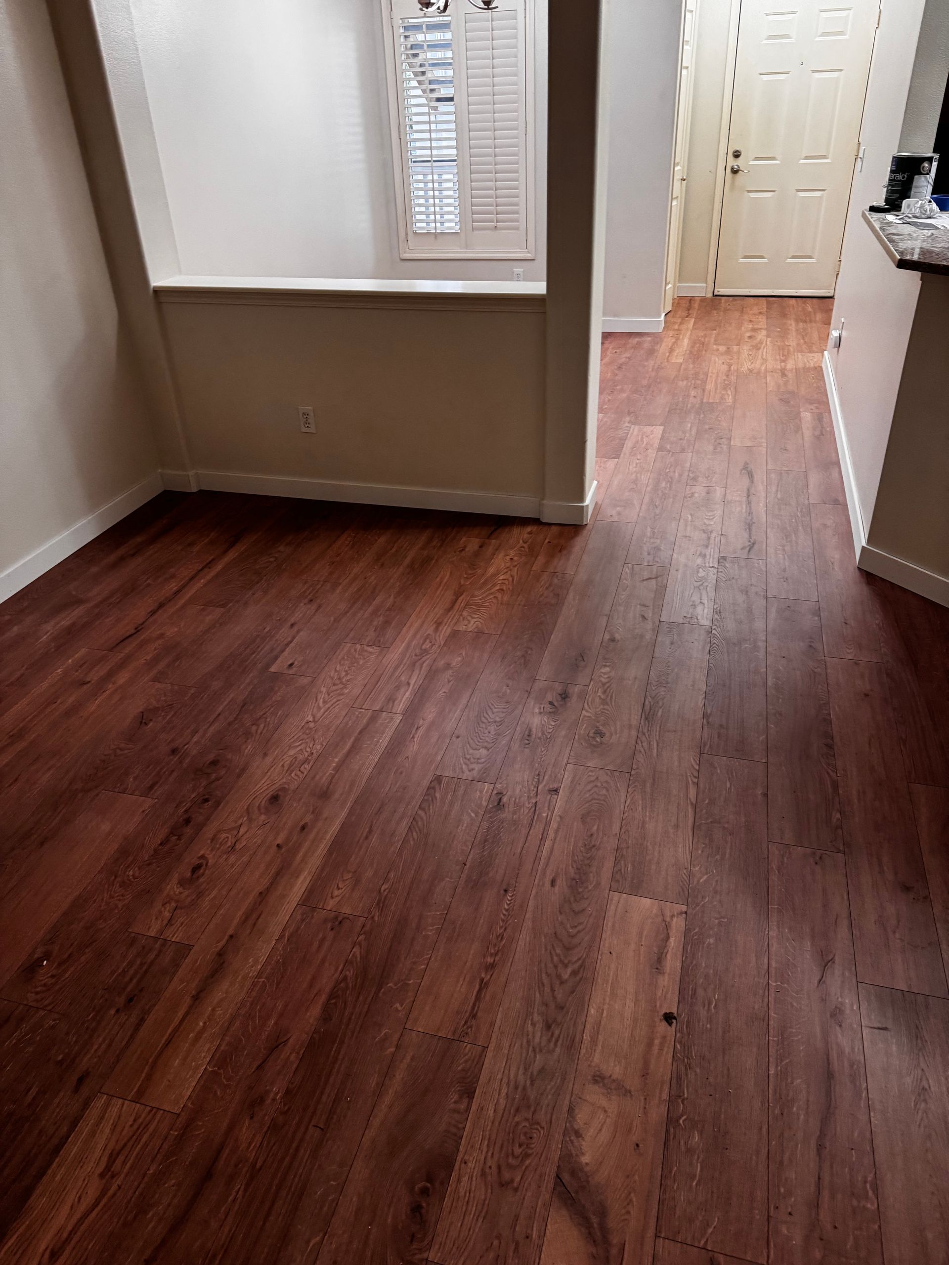 Dark wooden floor in a room, with a hallway and window visible.