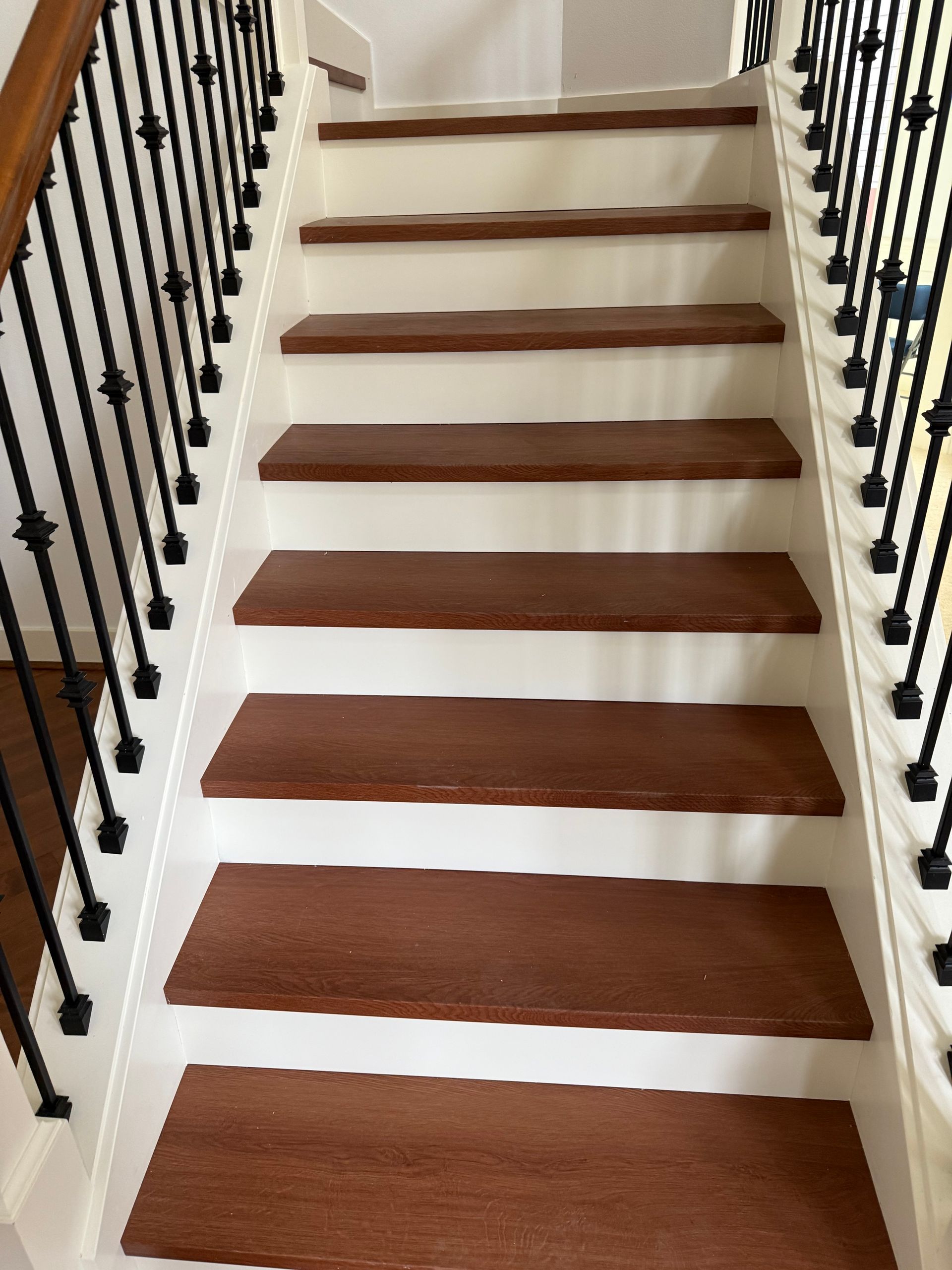 Staircase with brown treads, white risers, black spindles and wood handrail.