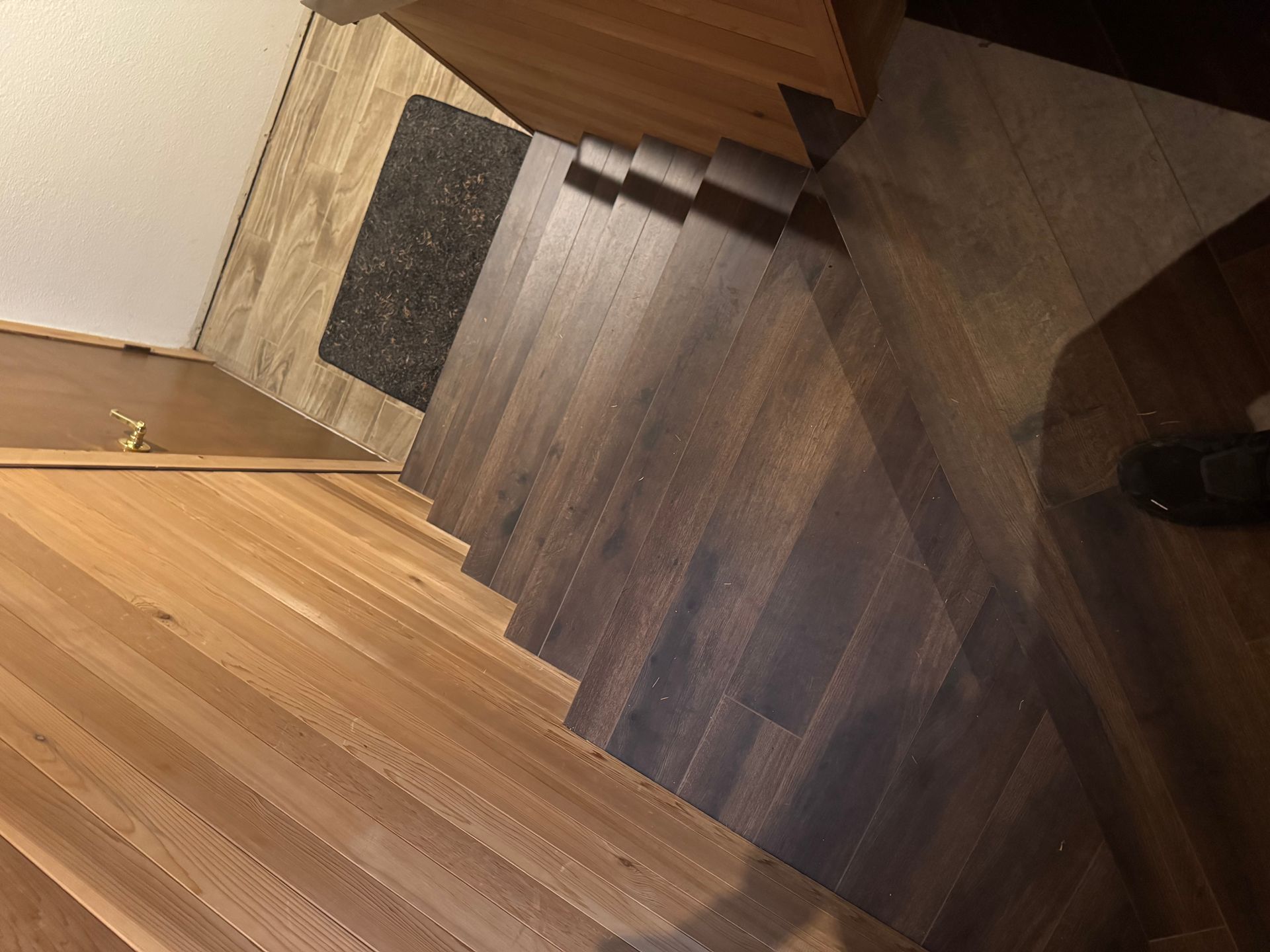 Wooden stairs with dark and light wood, leading downwards. A welcome mat is at the top.