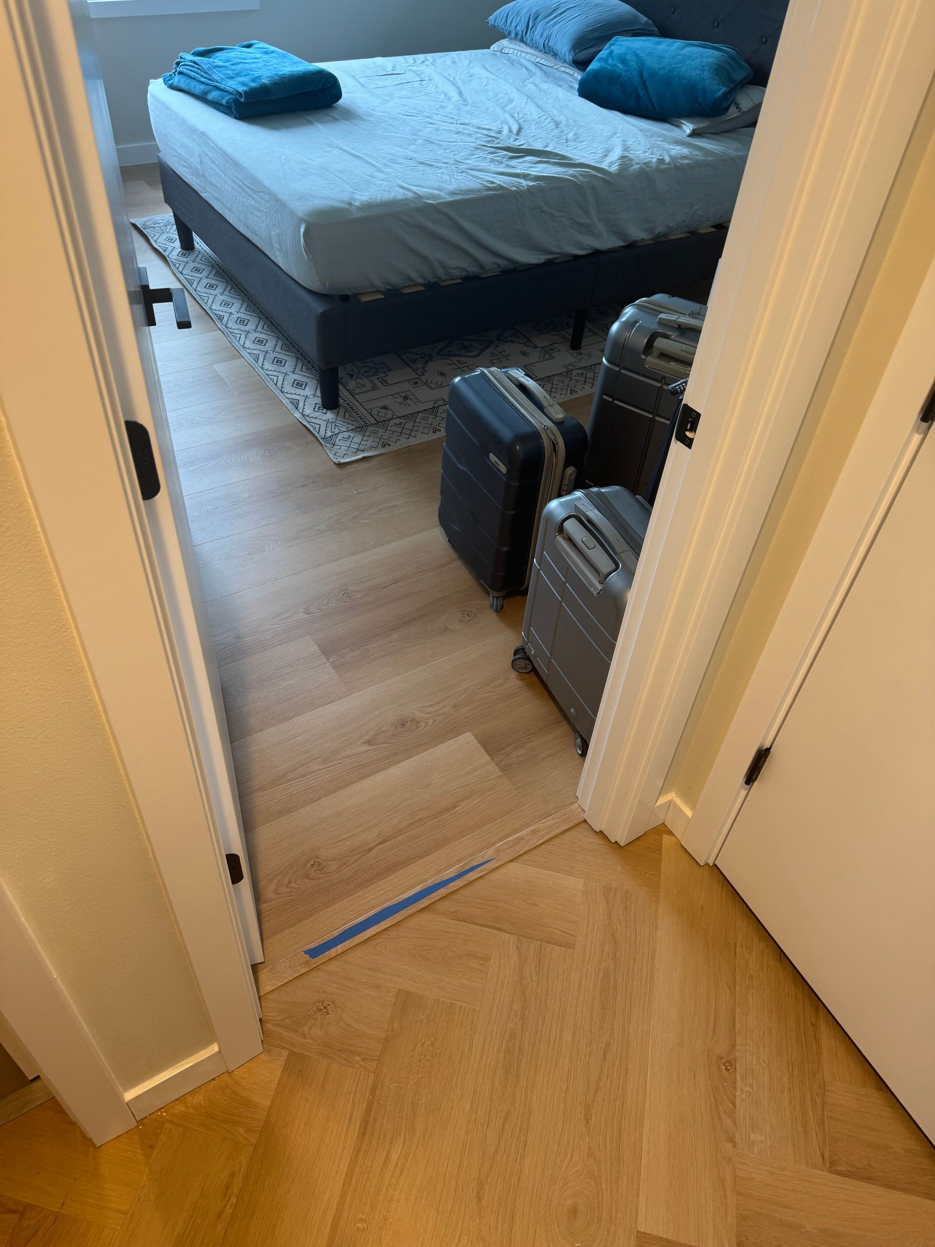 Bedroom interior with bed, luggage, and wood floor.