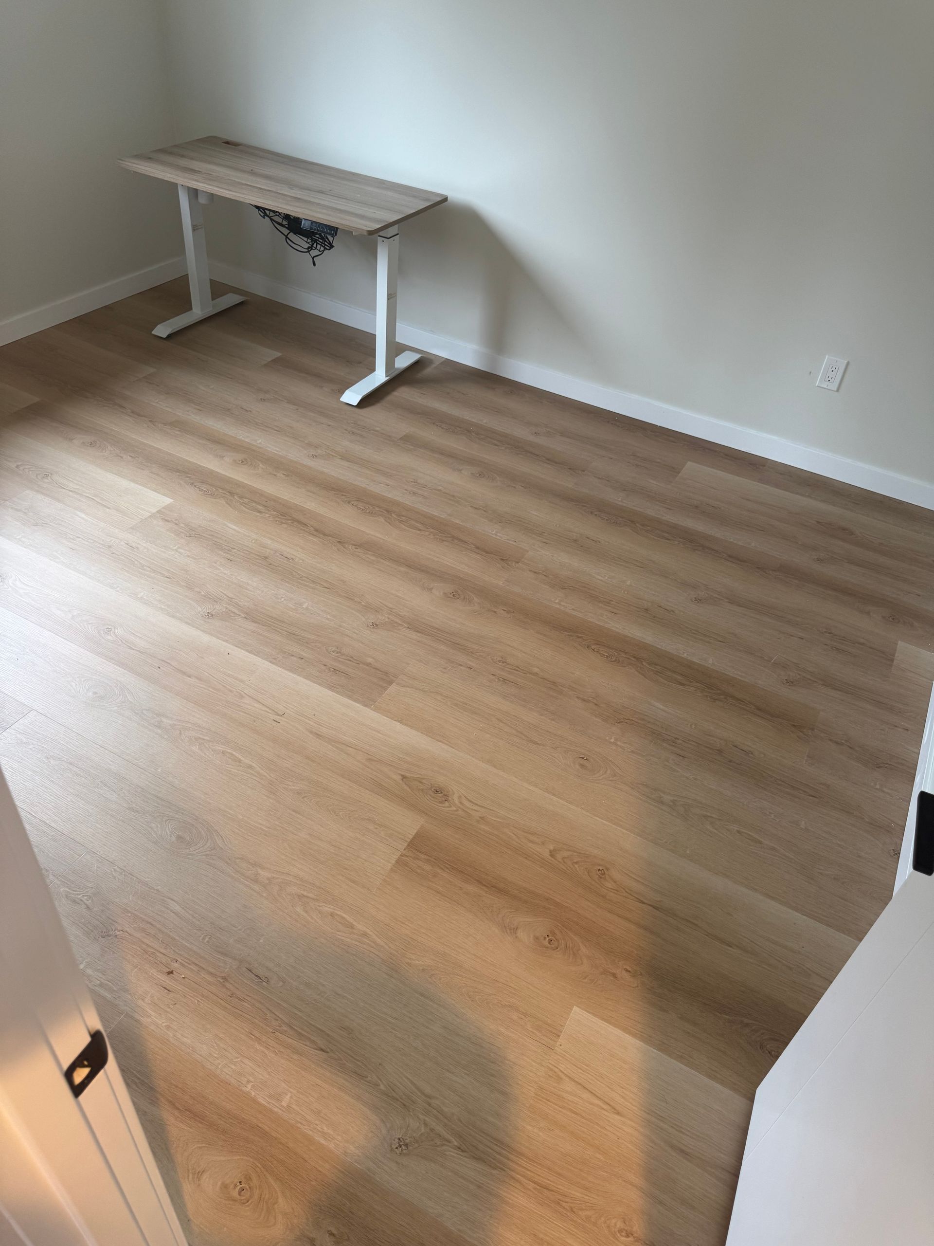 Room with light wood-look flooring and a height-adjustable desk against a white wall.