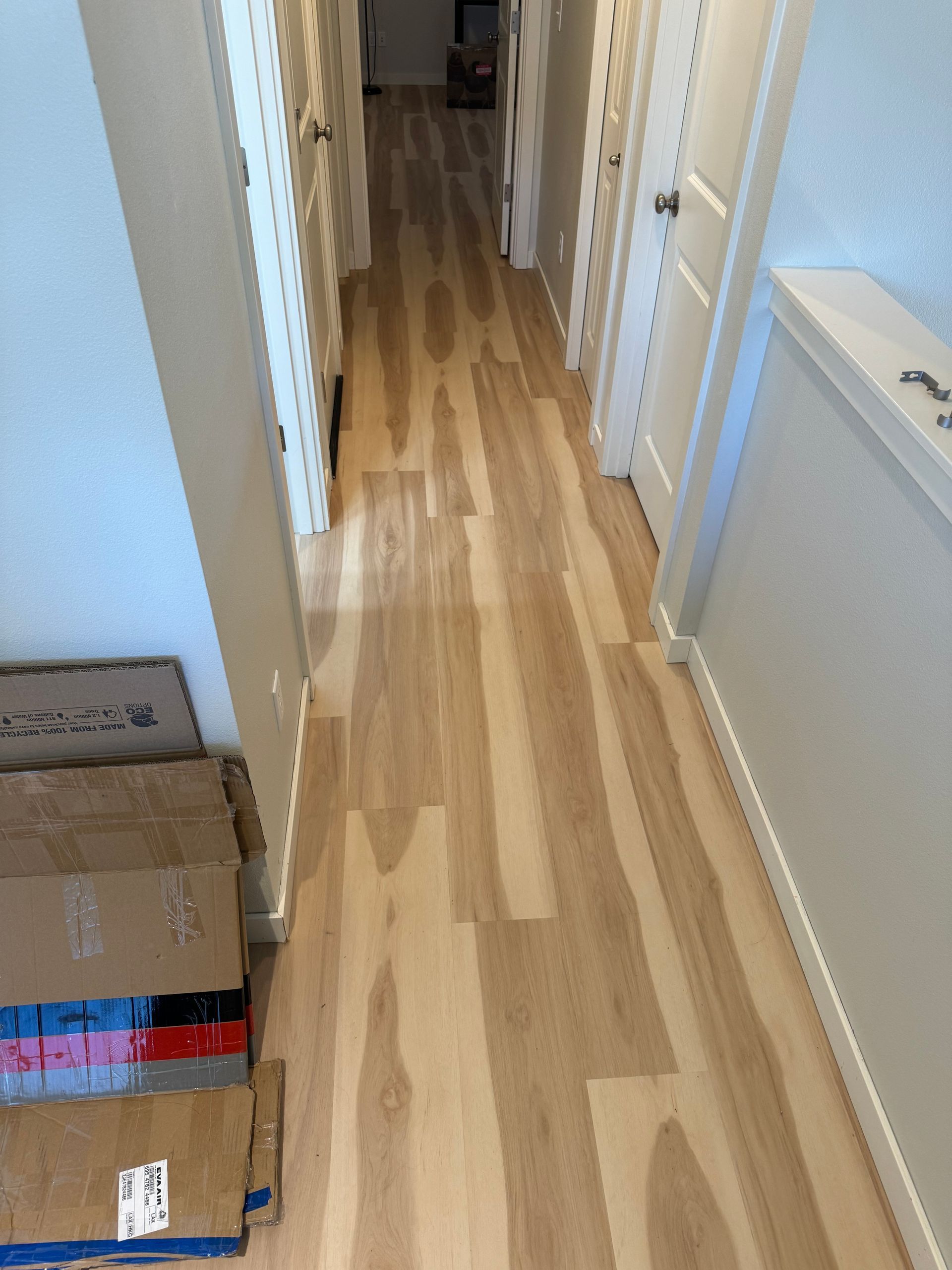 Hallway with light wood floors, white doors, and cardboard boxes on the left.