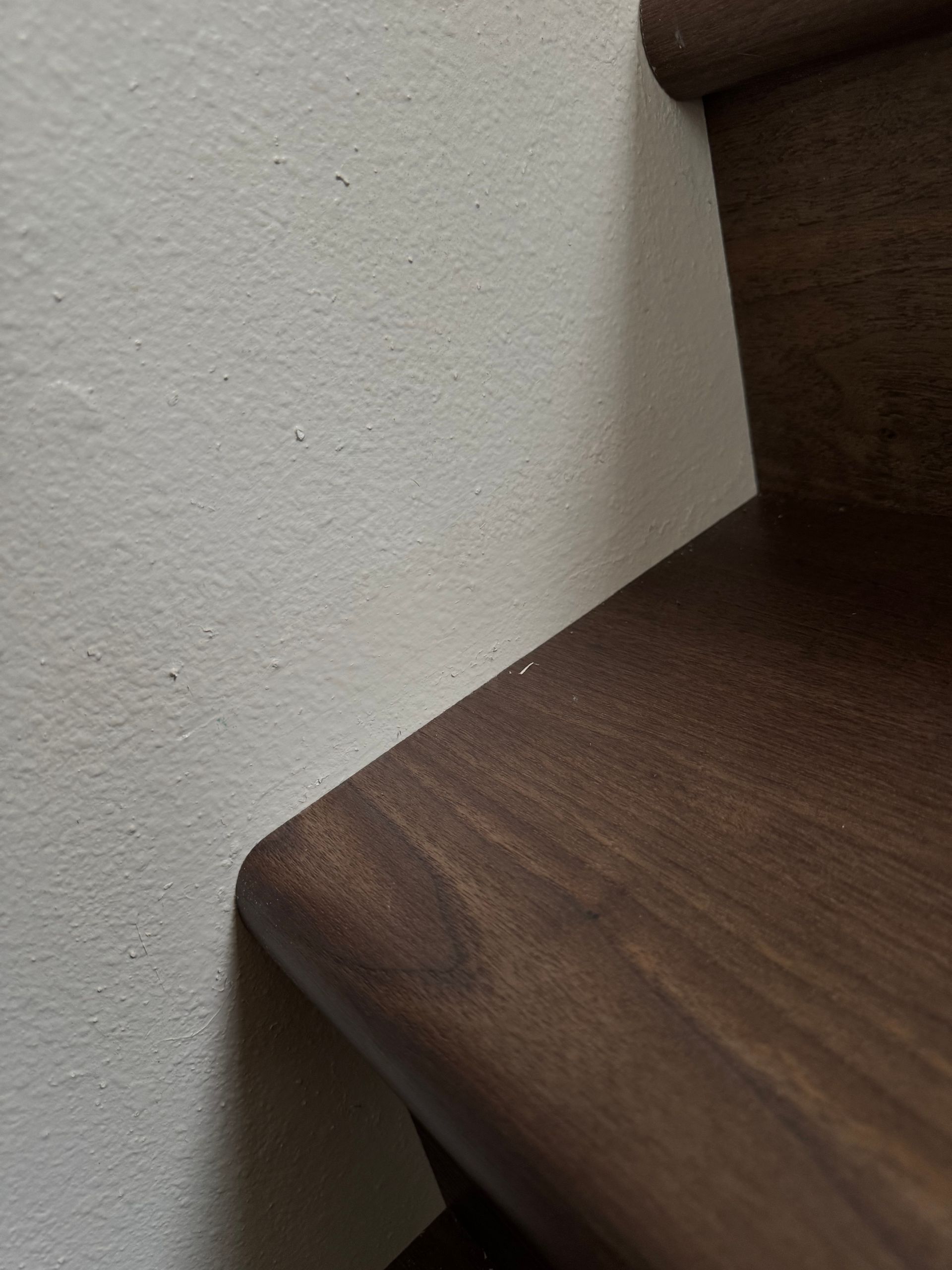 Wooden stair step next to a white wall. The step has a rounded edge.