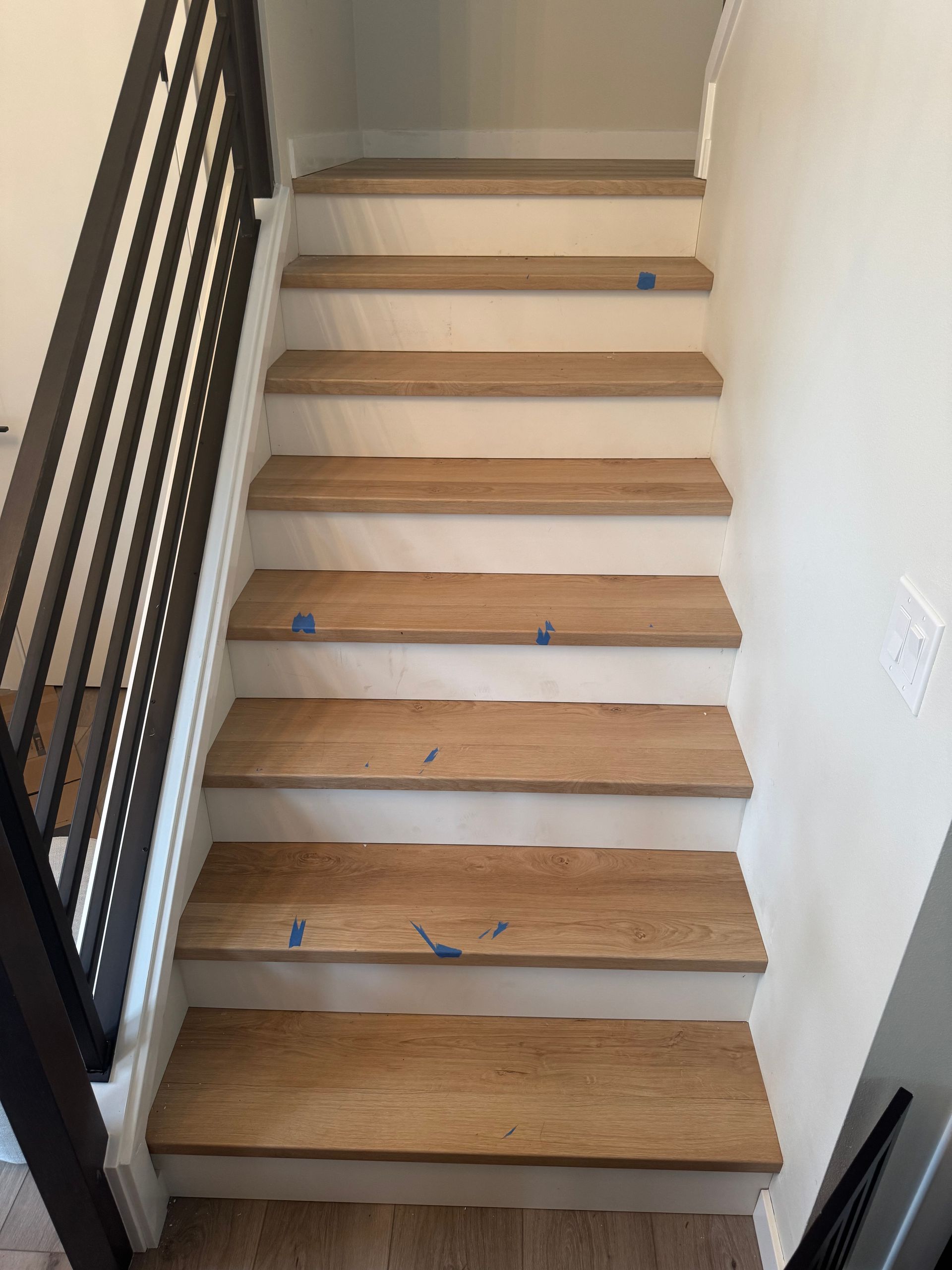 Wooden staircase with dark metal handrail against a white wall.