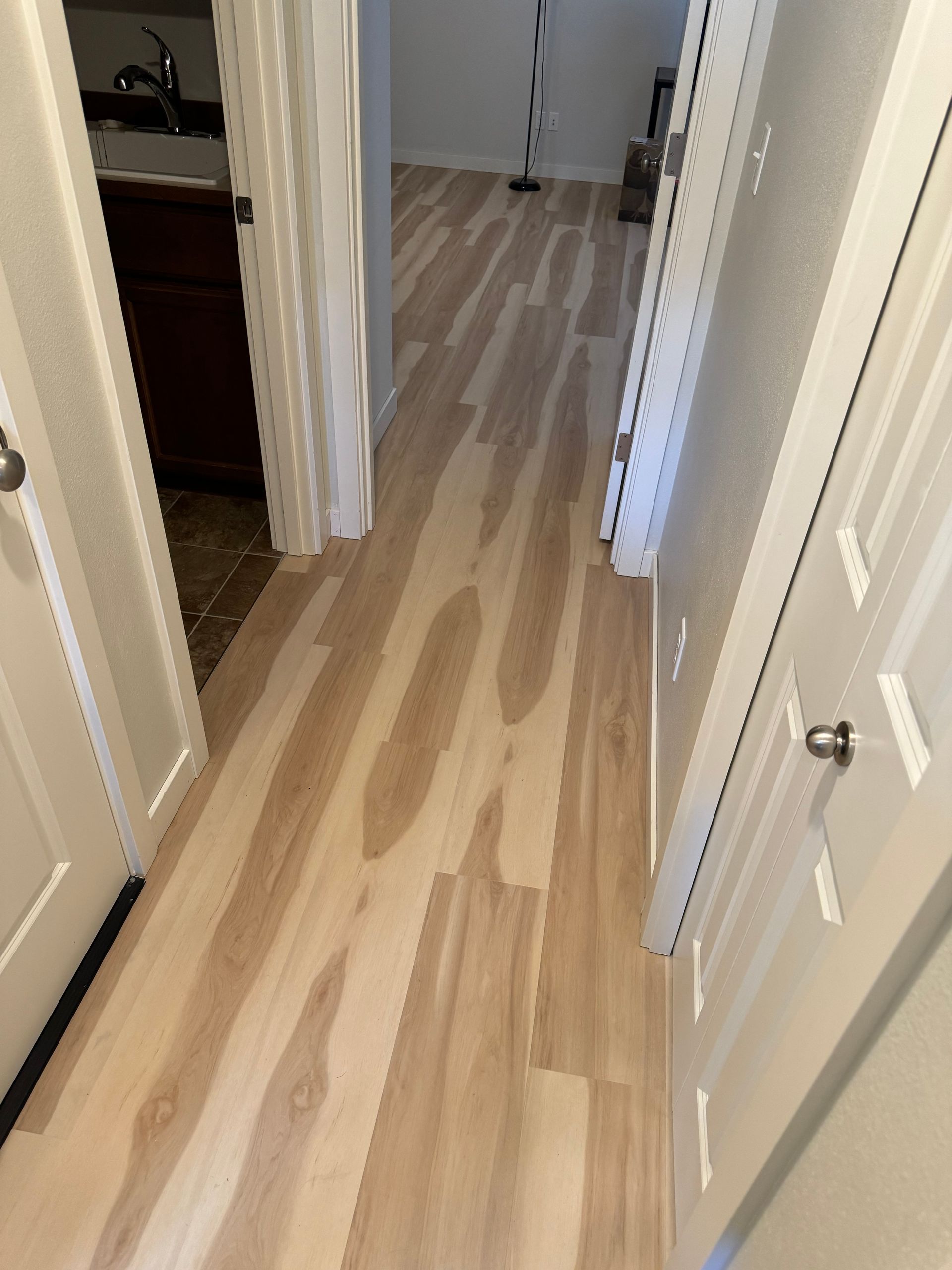 Hallway with light wood-look flooring, white doors, and a glimpse of a dark cabinet and countertop.