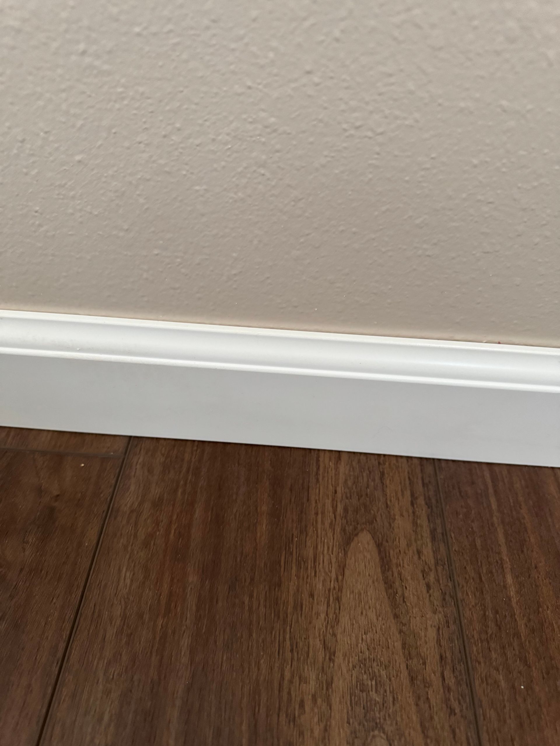 White baseboard trim on a dark wood floor, cream-colored wall above.