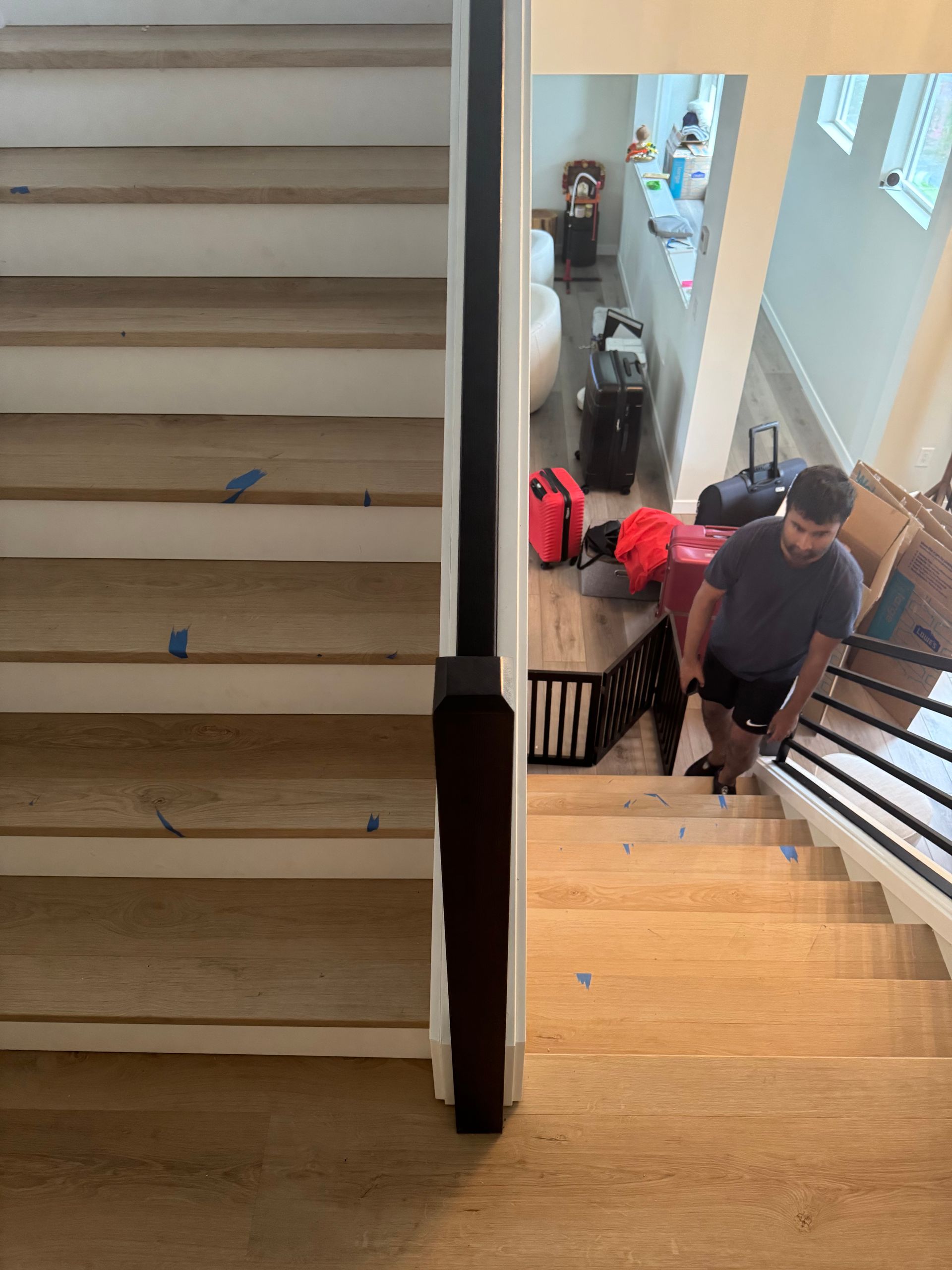 A person carries luggage up a wooden staircase. A black railing runs alongside the stairs.