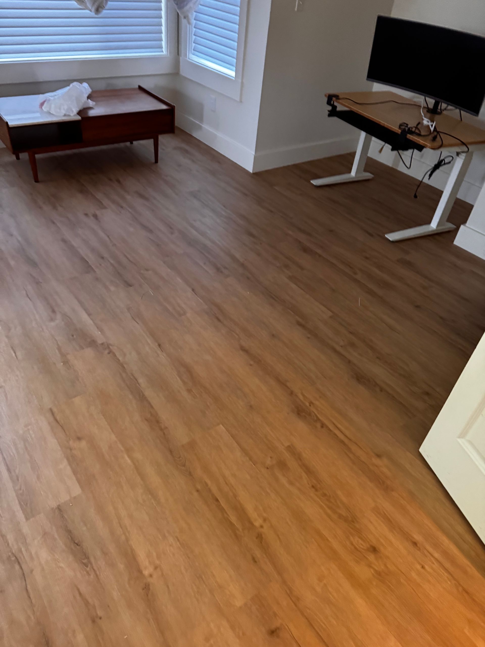 Room with wood-look flooring, a coffee table, and a desk with a computer monitor.