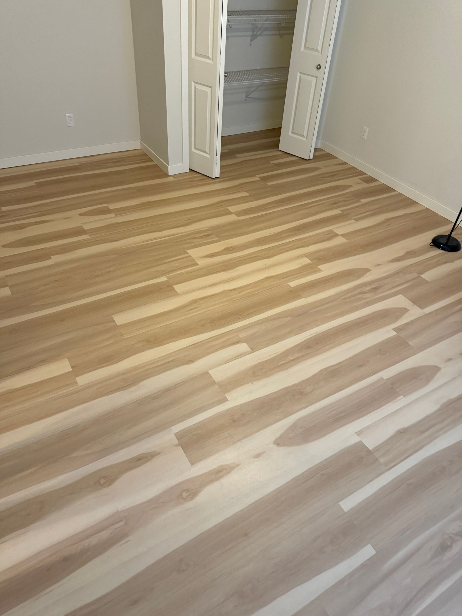 Light wood-look flooring installed in a room, with white walls and a partially open closet door.
