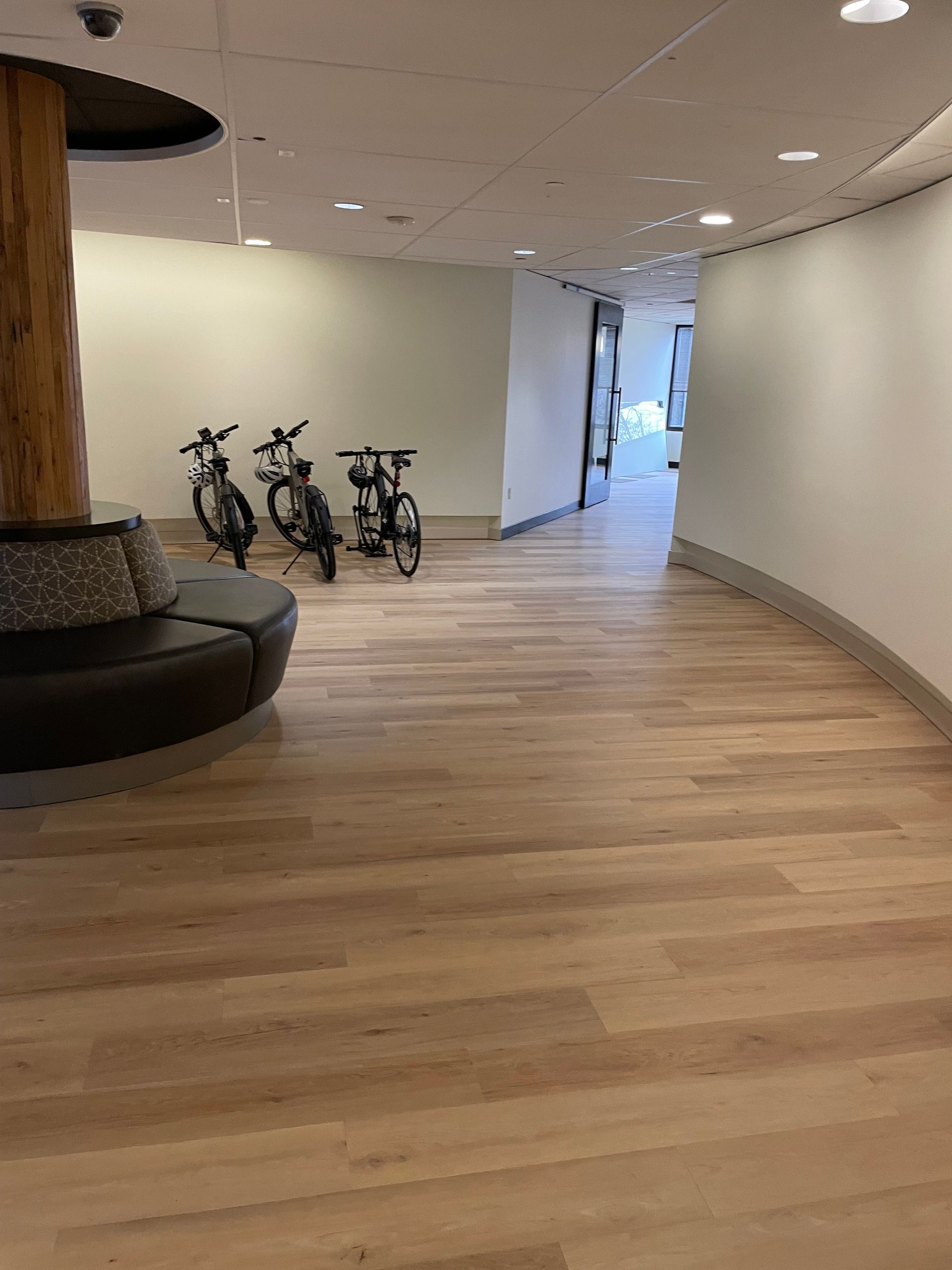 Hallway with wood floors, curved white walls, and three bicycles parked near a round black sofa.
