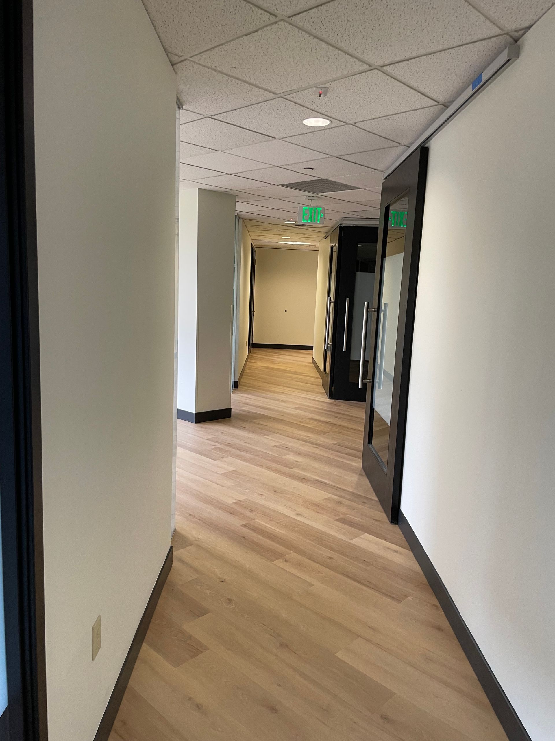 Hallway with light wood floors, white walls, and open doorways.