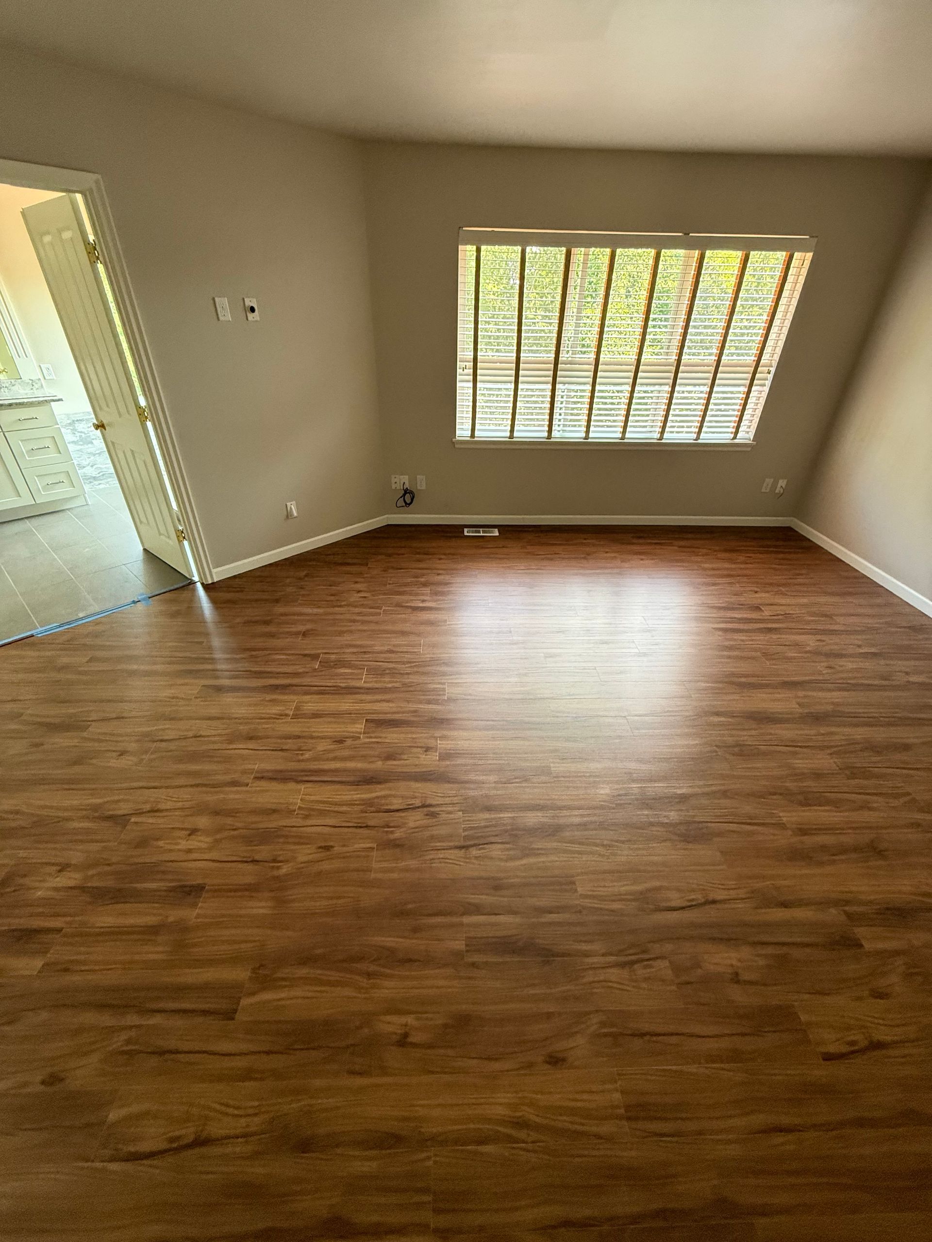 Empty room with wood-look flooring, a window, and an open doorway to another room.