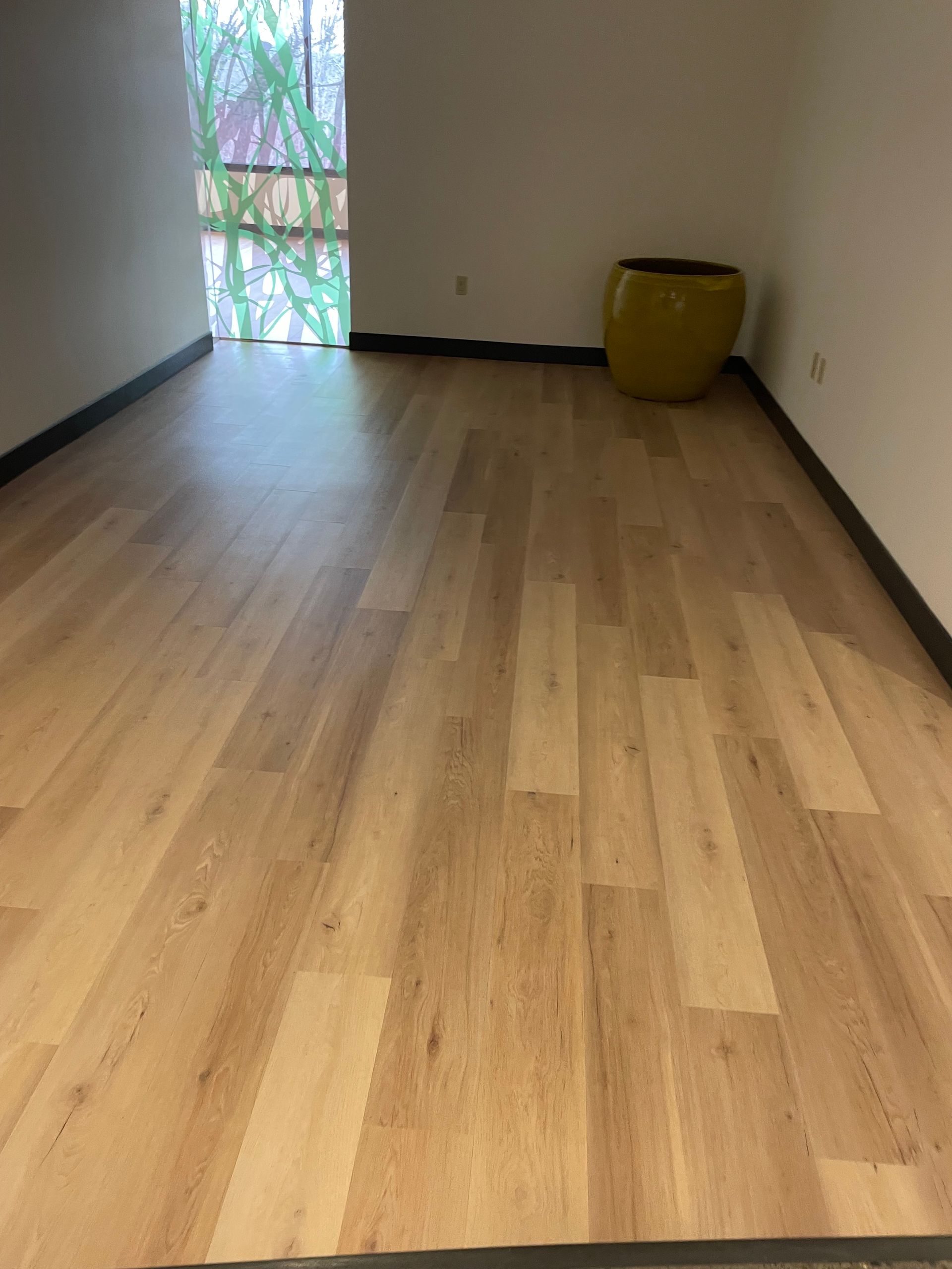 Light wood-look flooring in a room with a yellow pot. Window with green outside.